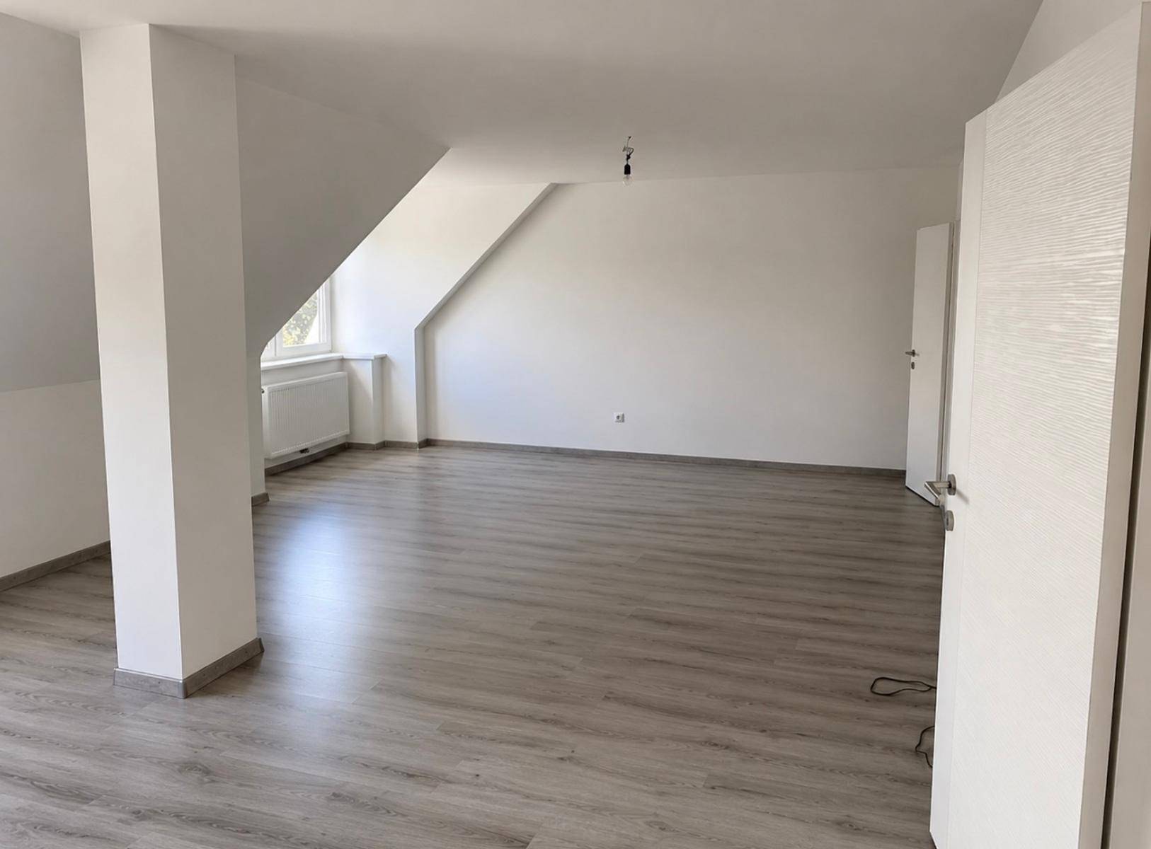 Geräumiger, unmöblierter Raum im Dachgeschoss mit modernem Bodenbelag und Dachschräge.