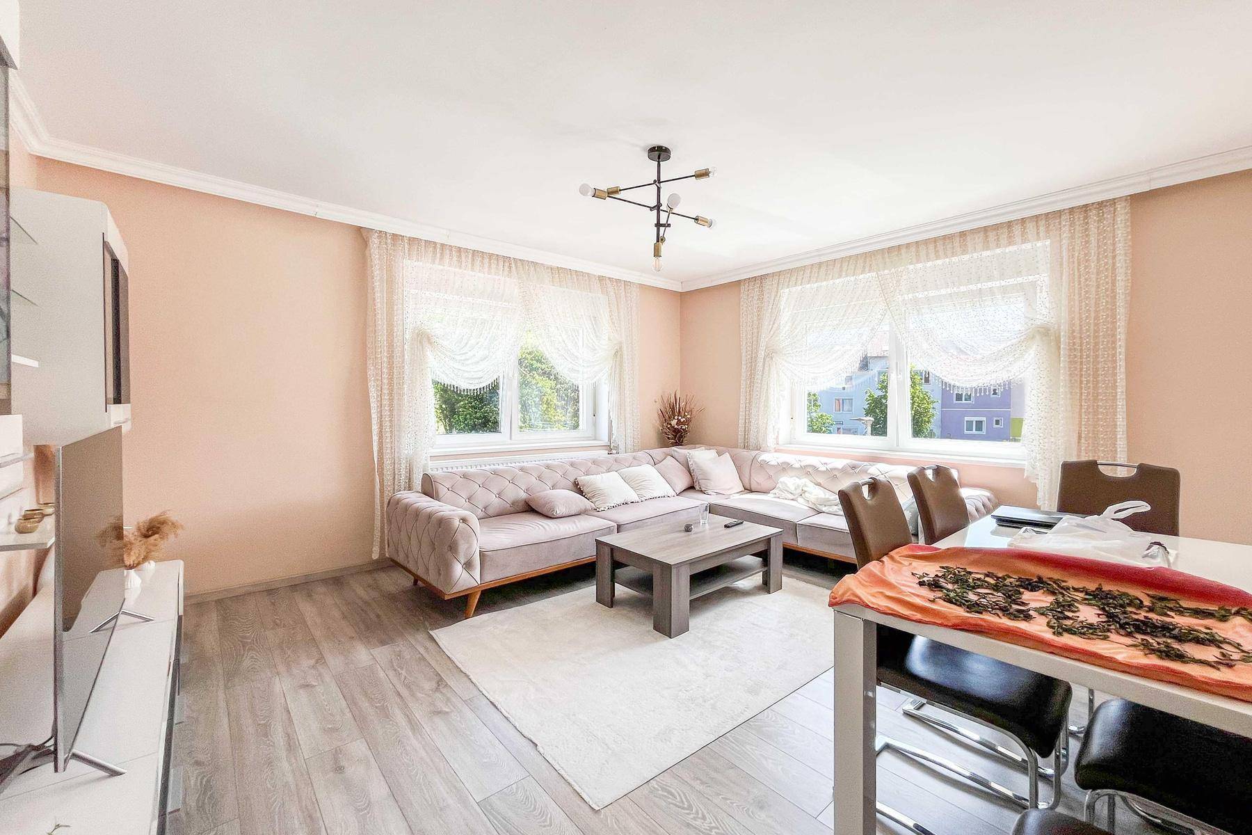 Geräumiger Wohn- und Essbereich mit beigem Sofa, modernem Boden und großen Fenstern.
