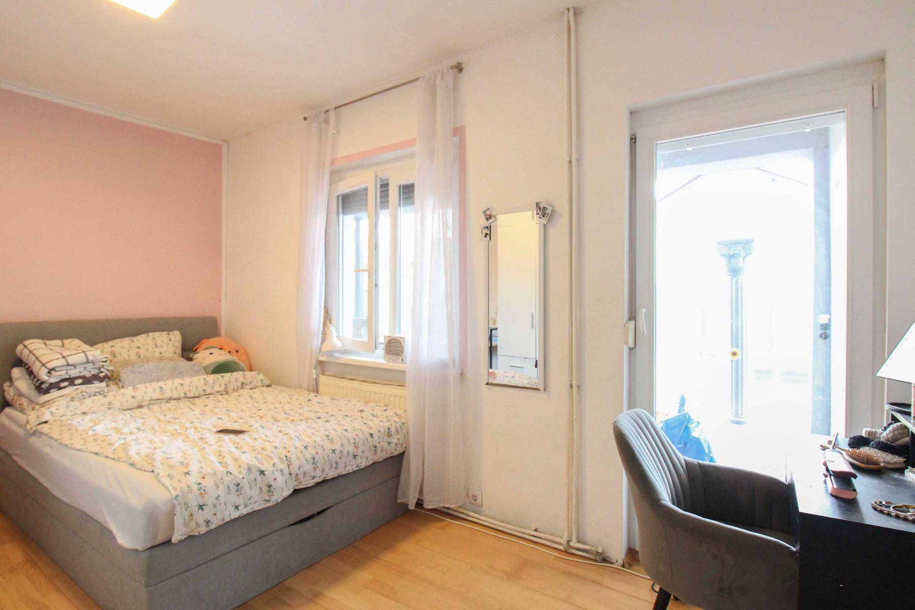 Helles Schlafzimmer mit Holzboden, Fenster und Zugang zu einem Außenbereich.