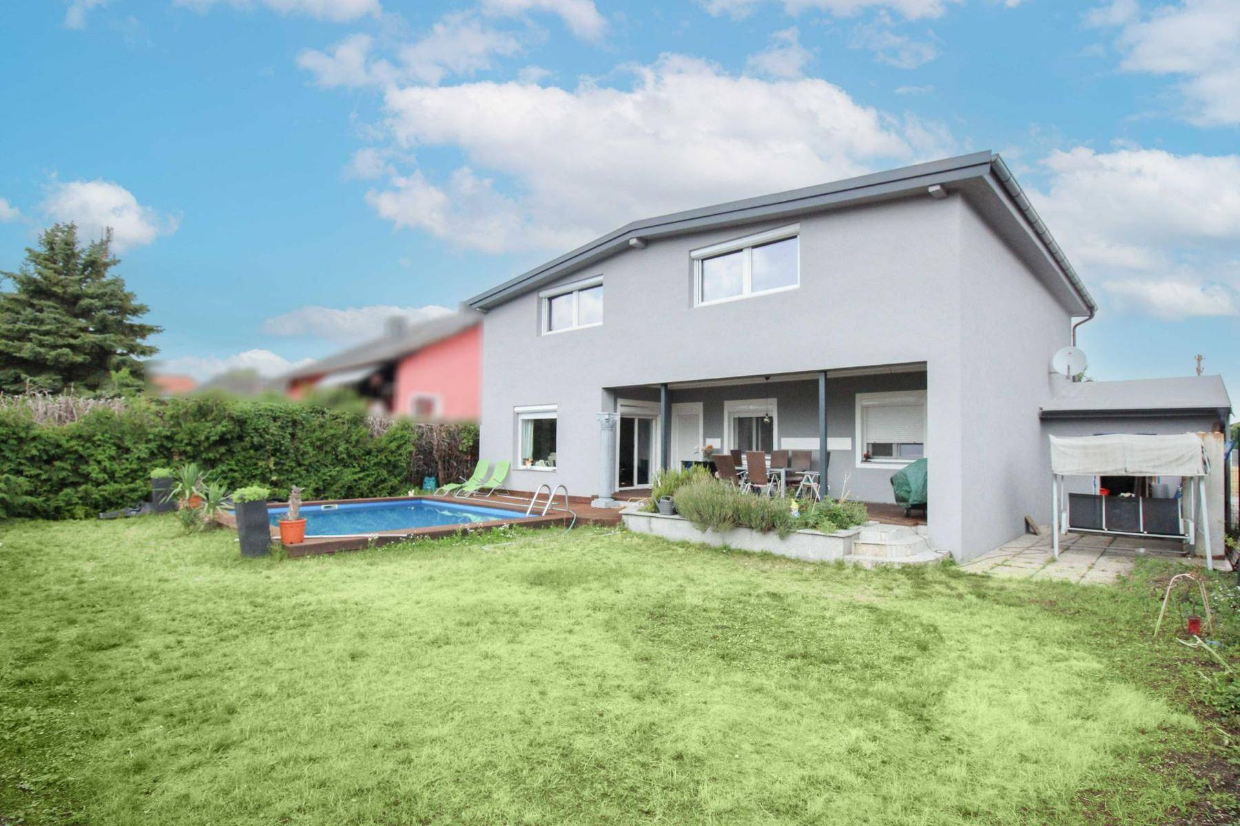 Rückansicht des Hauses mit Pool, großer Rasenfläche und überdachter Terrasse.