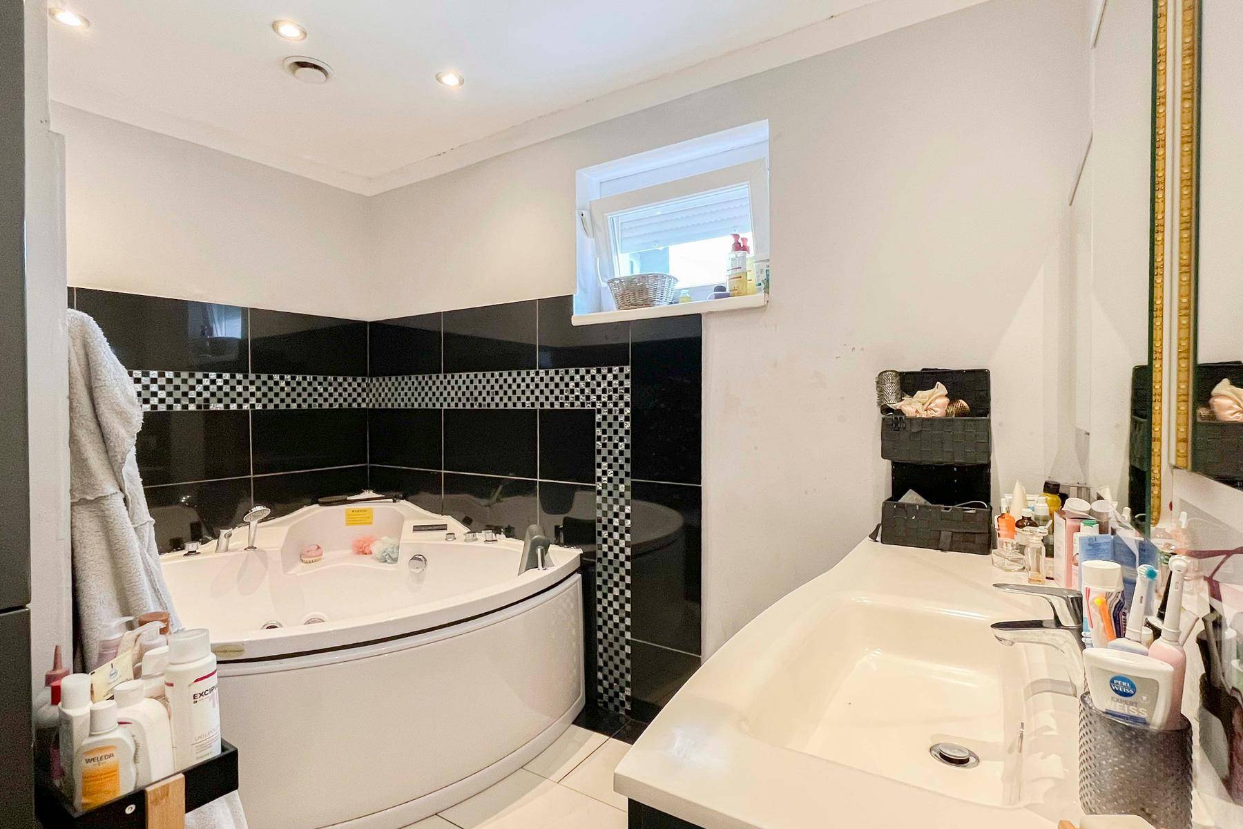Modernes Badezimmer mit Eckbadewanne, Doppelwaschbecken und schwarzen Fliesen.