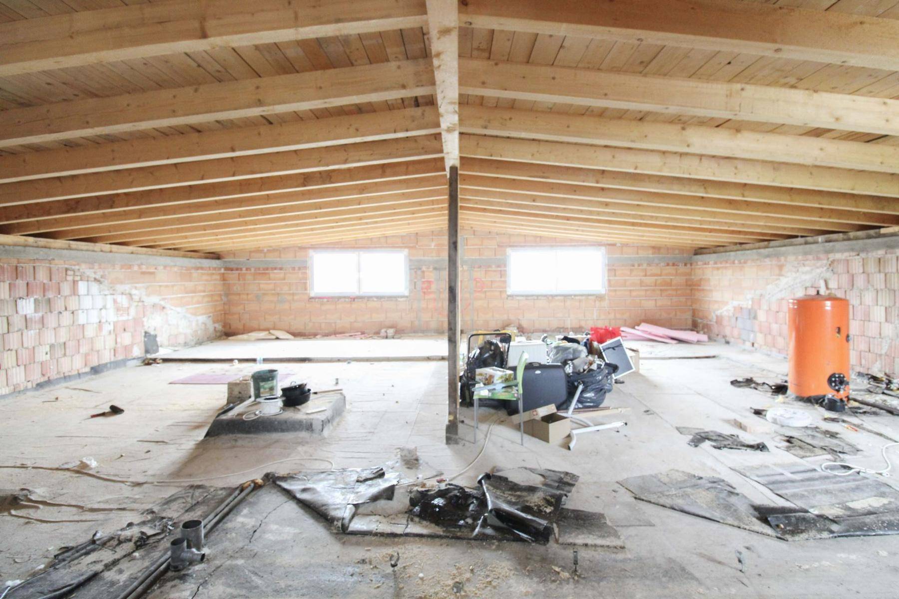 Geräumiger Dachboden im Rohbau mit sichtbaren Holzbalken und Fenstern.