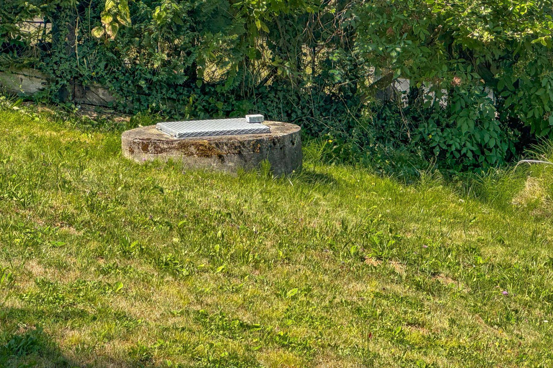 Ein runder Betonschacht mit Metallabdeckung in einer grünen Rasenfläche.