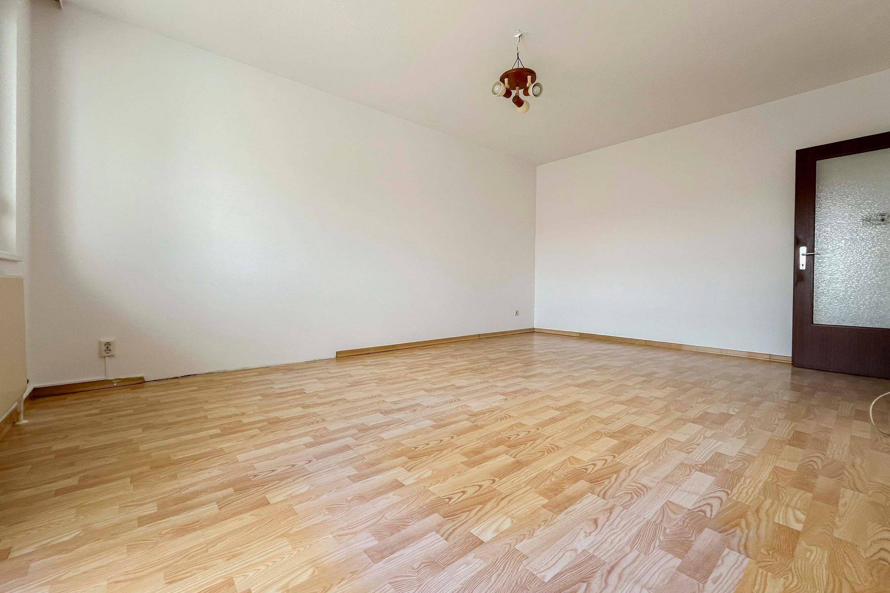 Geräumiger, leerer Raum mit hellem Laminatboden und einer Tür mit Milchglas, vielseitig nutzbar.