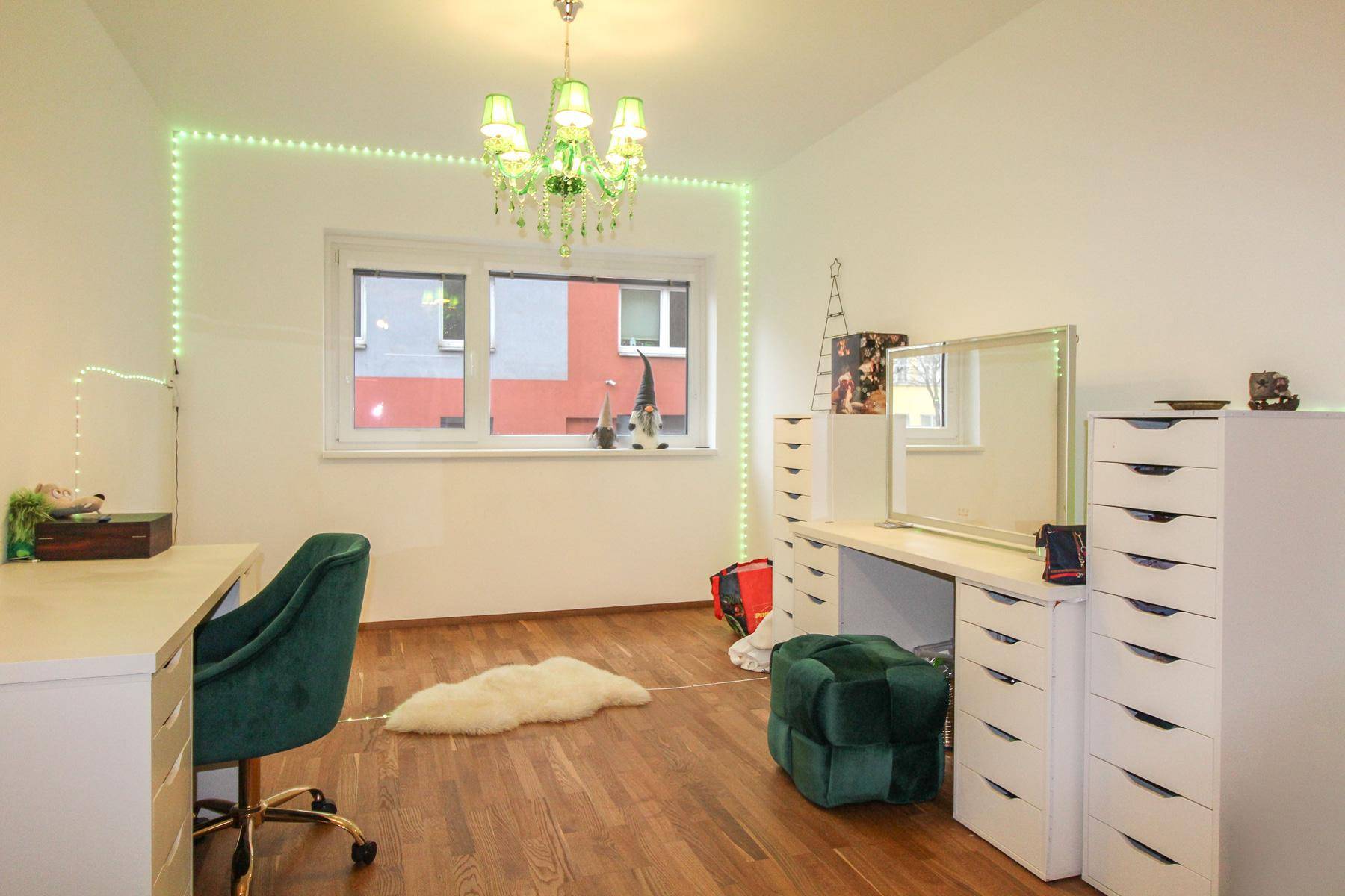 Helles Ankleidezimmer mit Fenster, Schminktisch und einem markanten grünen Kronleuchter.