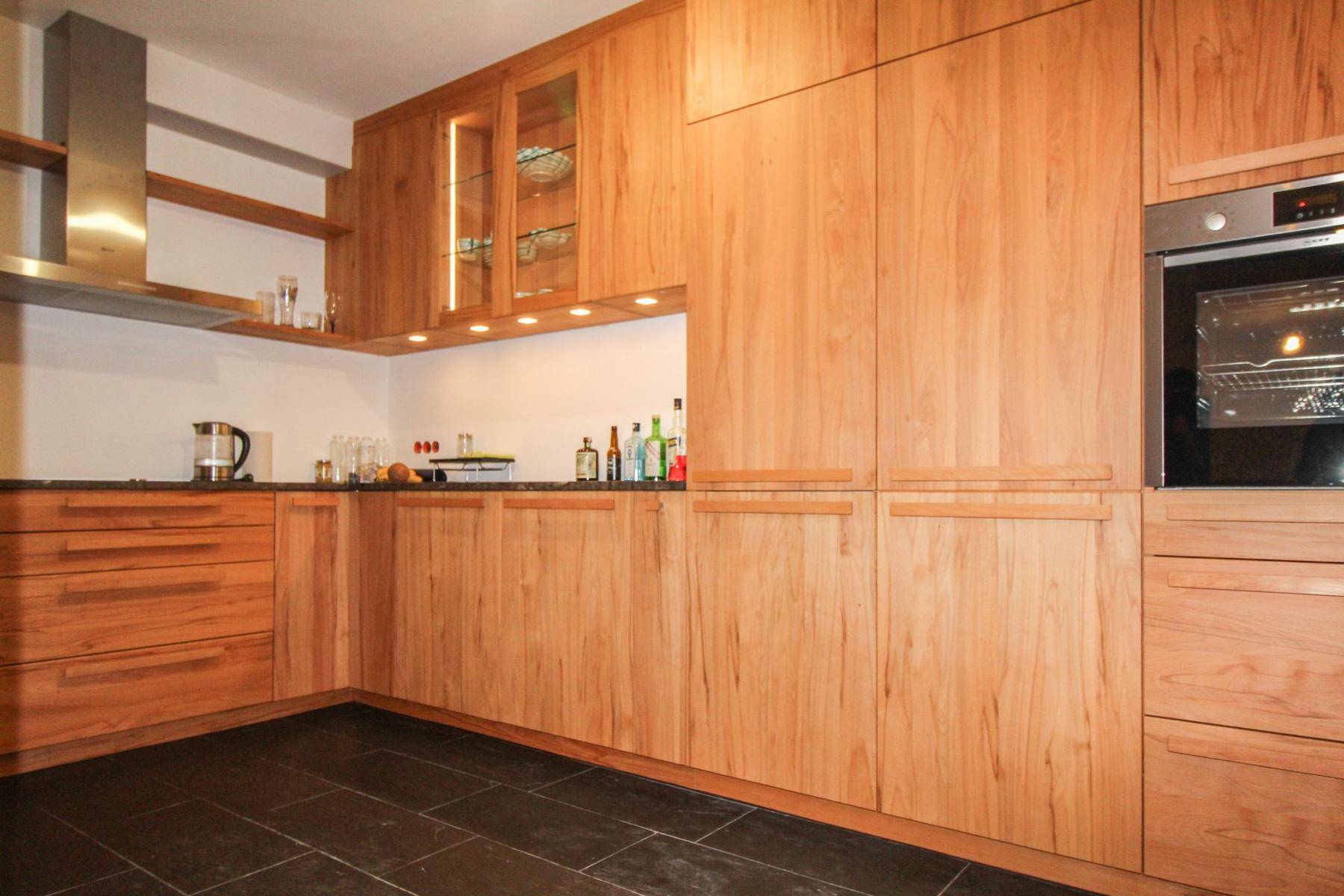 Moderne Küche mit Holzfronten, dunkler Arbeitsplatte und schwarzen Fliesenboden.