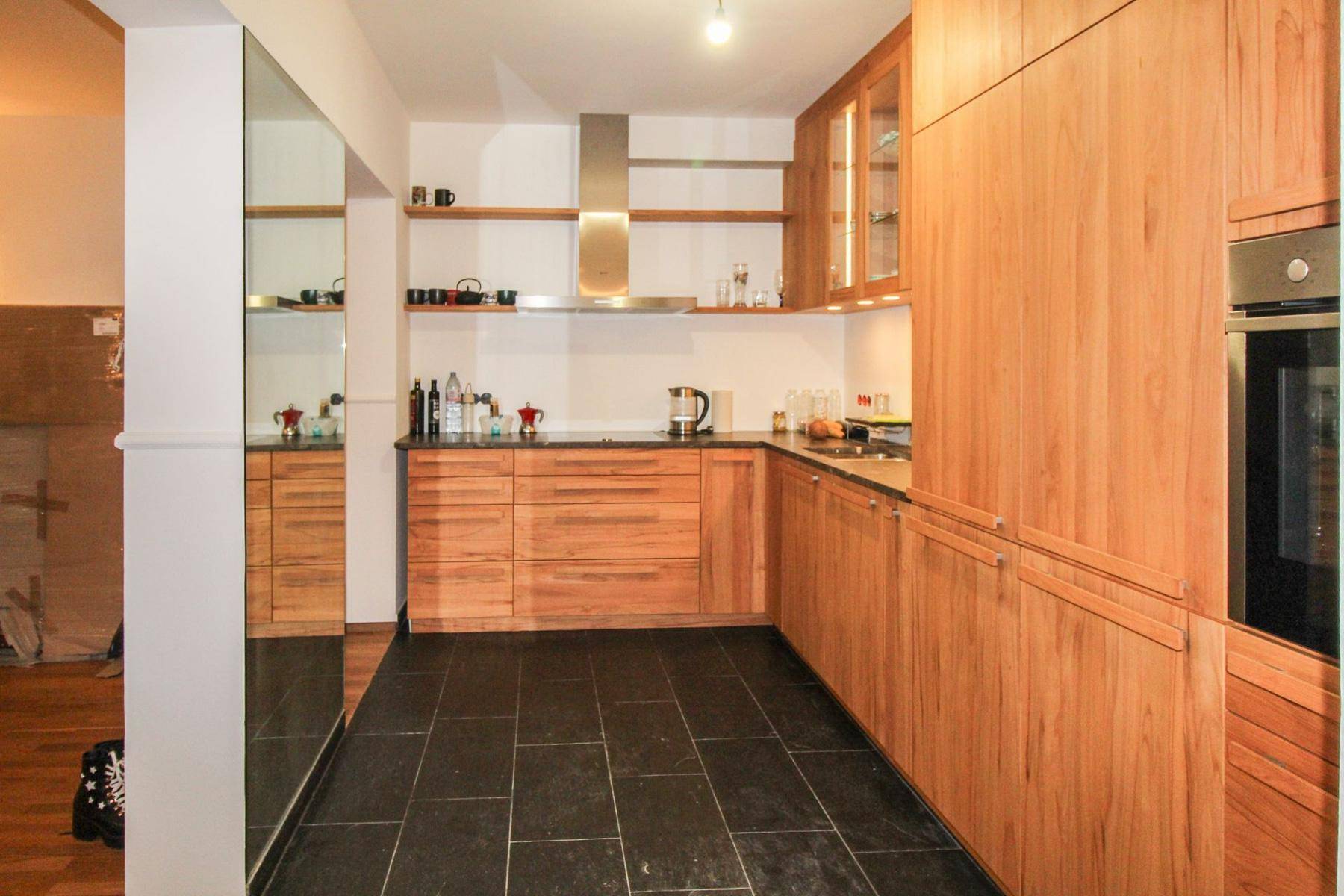 Geräumige Küche mit Holzschränken, schwarzem Fliesenboden und einer großen Spiegelfläche.