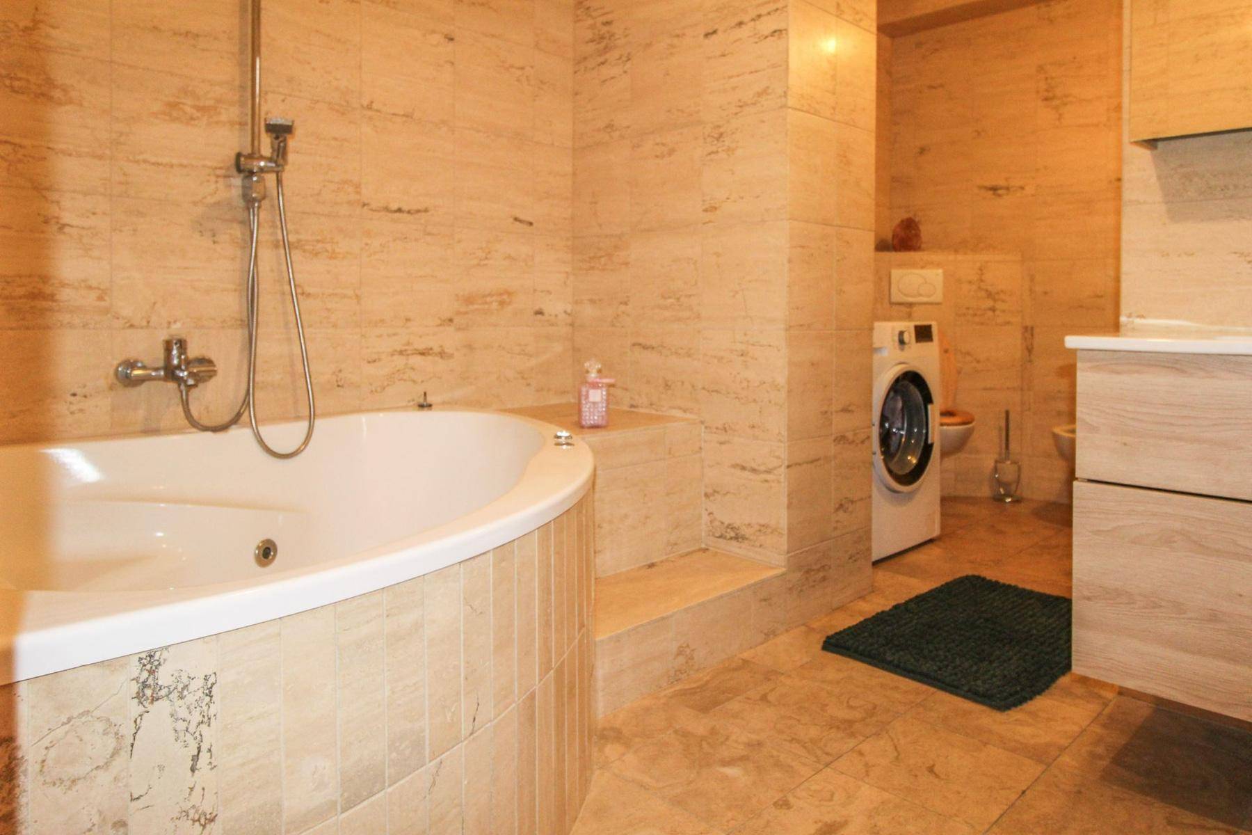 Helles Badezimmer mit beigefarbenen Fliesen, Eckbadewanne mit Dusche und Waschmaschine.