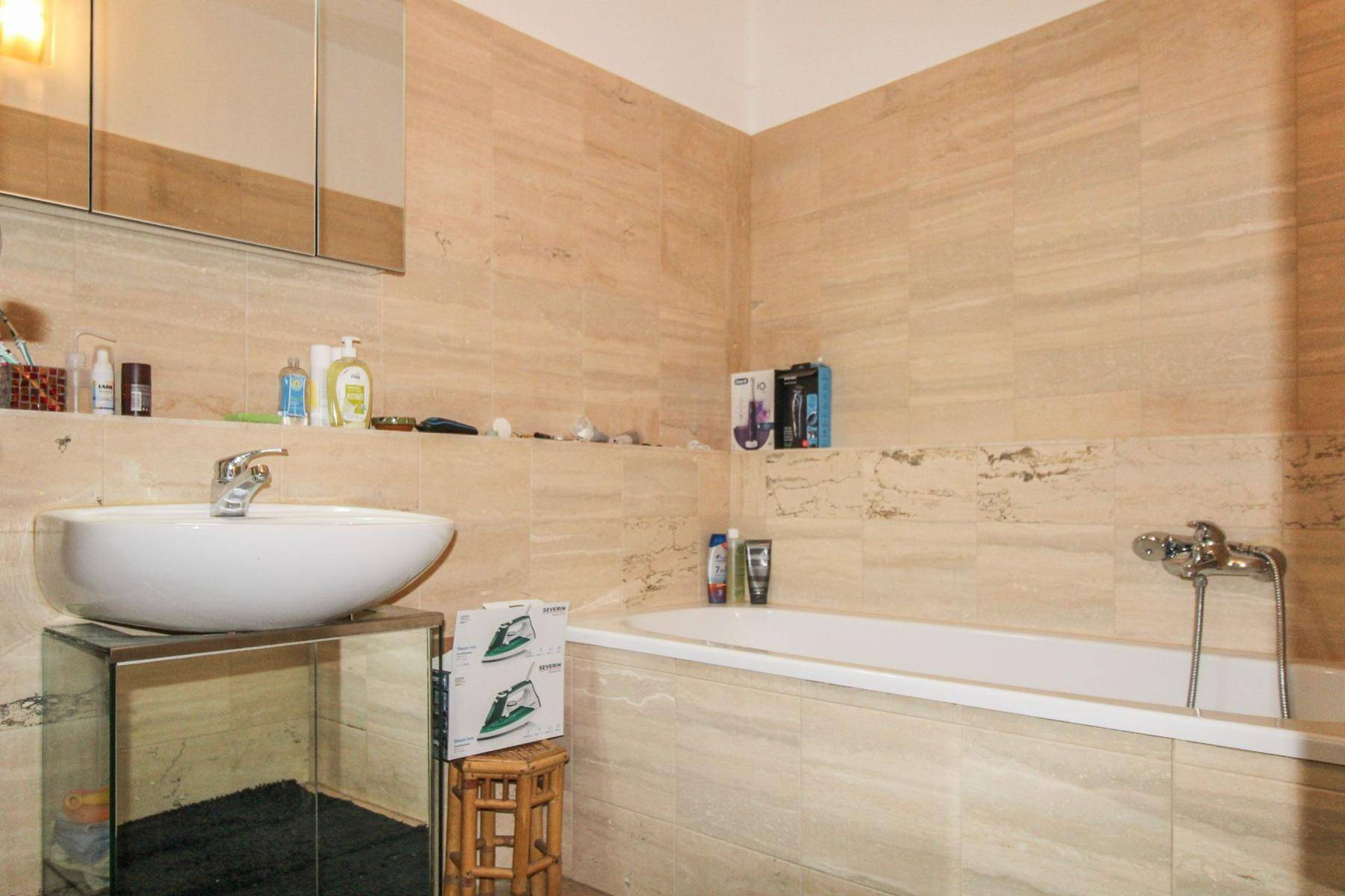 Badezimmer mit beigefarbenen Fliesen, Waschbecken auf Waschtisch und einer Badewanne.