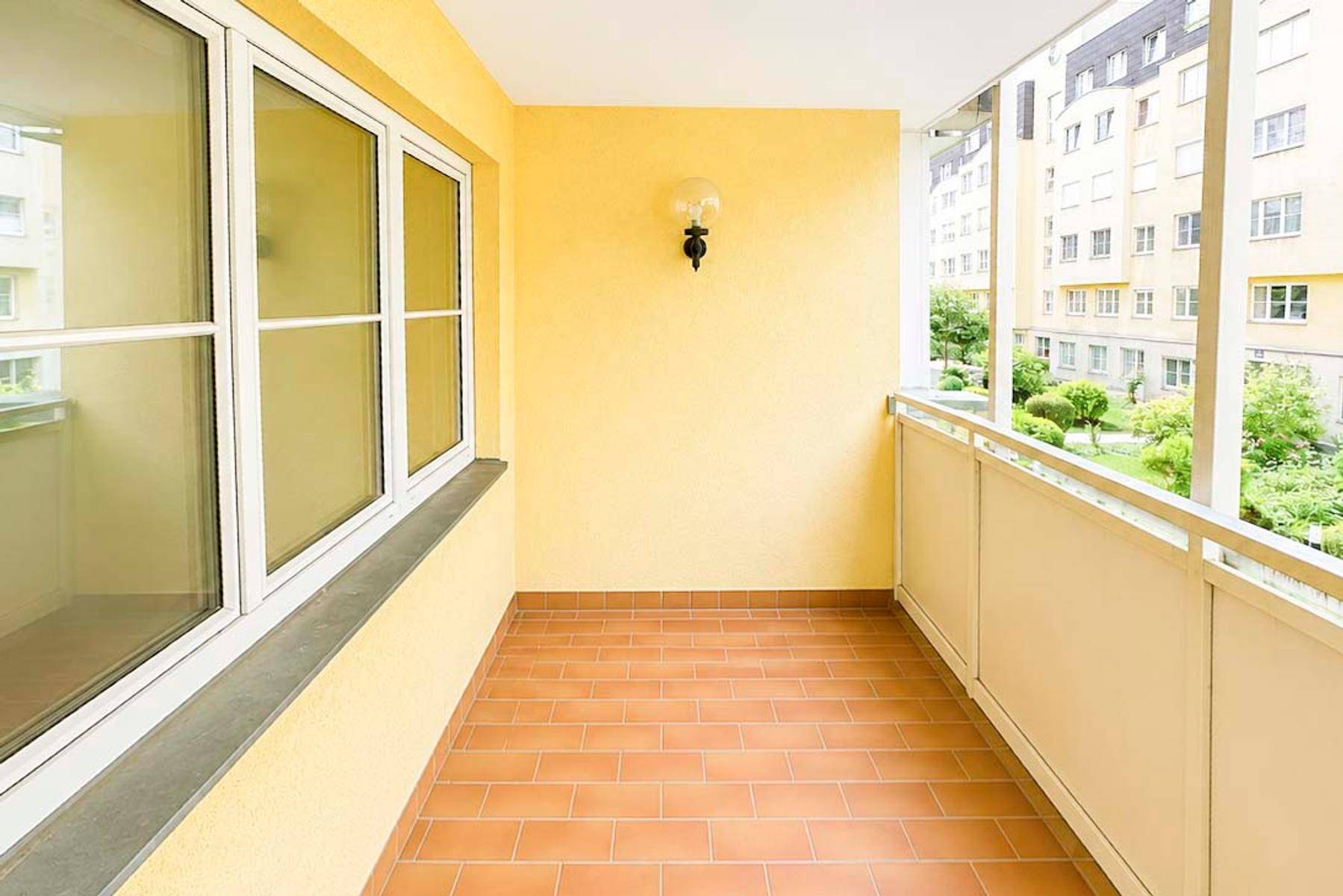 Heller Balkon mit Terrakottafliesen und gelben Wänden, bietet Blick auf den grünen Innenhof.