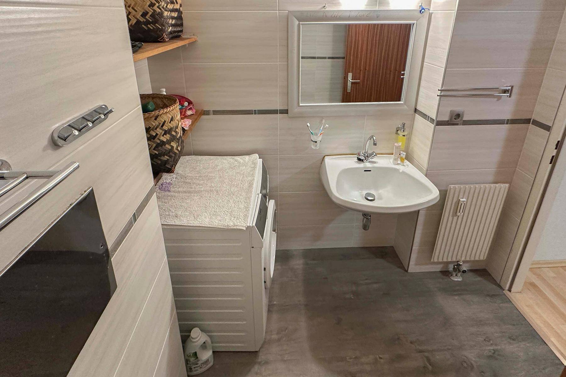 Helles Badezimmer mit Waschbecken, Spiegel, Waschmaschine und beheiztem Handtuchhalter.