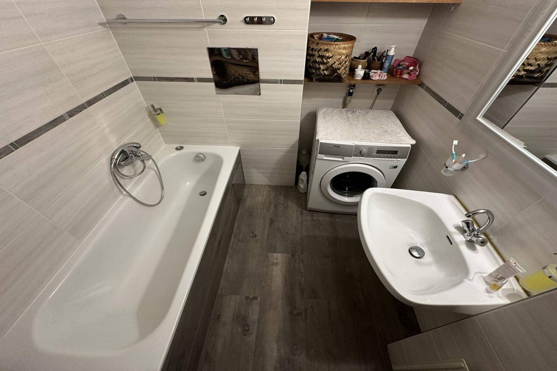 Modernes Badezimmer mit Badewanne, Waschbecken und Waschmaschine, hell gefliest.