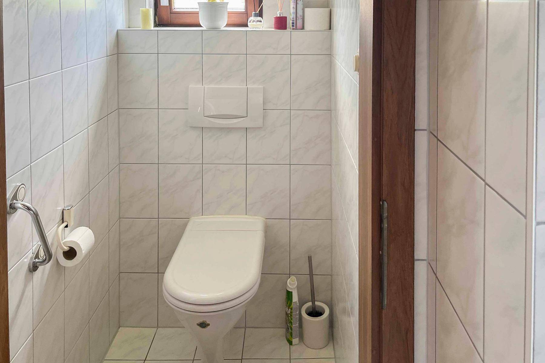 Kleines Gäste-WC mit weißen Fliesen, wandhängendem WC und Fenster.
