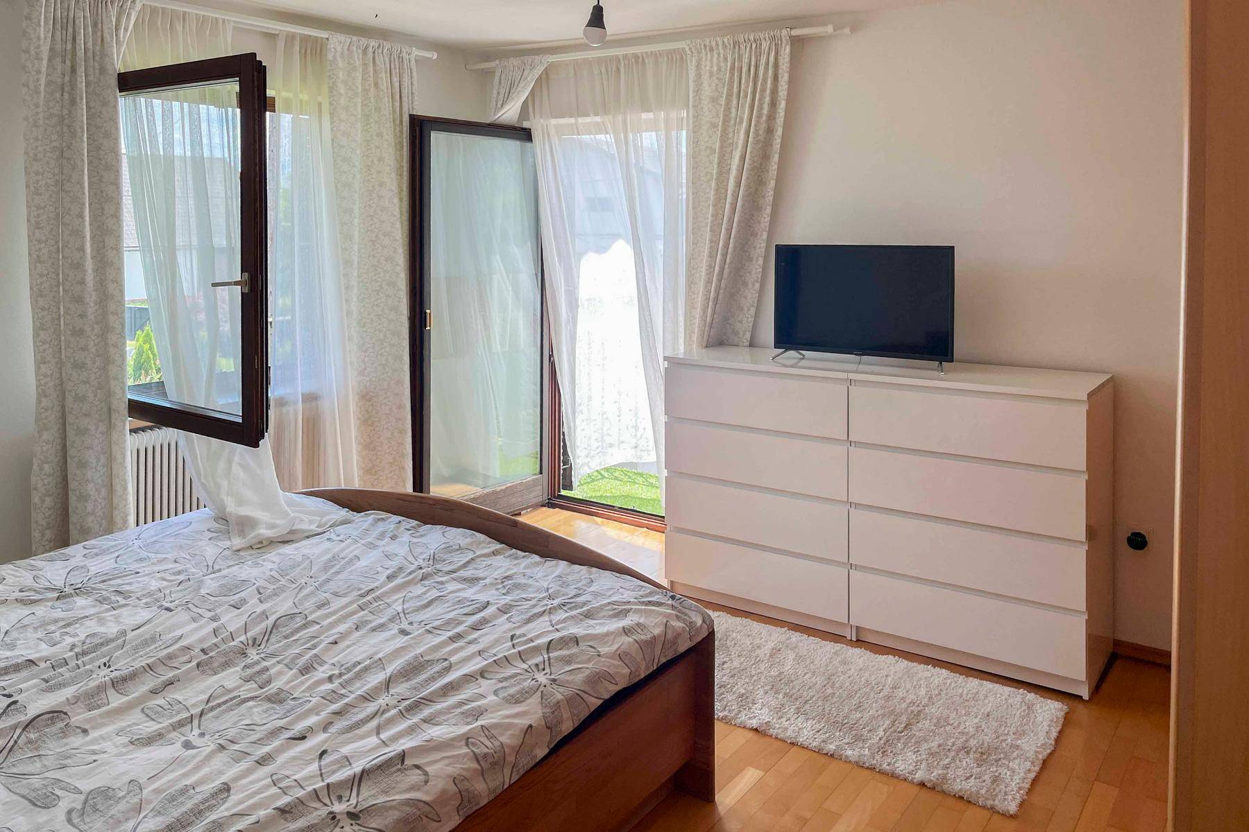 Helles Schlafzimmer mit Holzboden, weißer Kommode und Zugang zu einem Außenbereich.