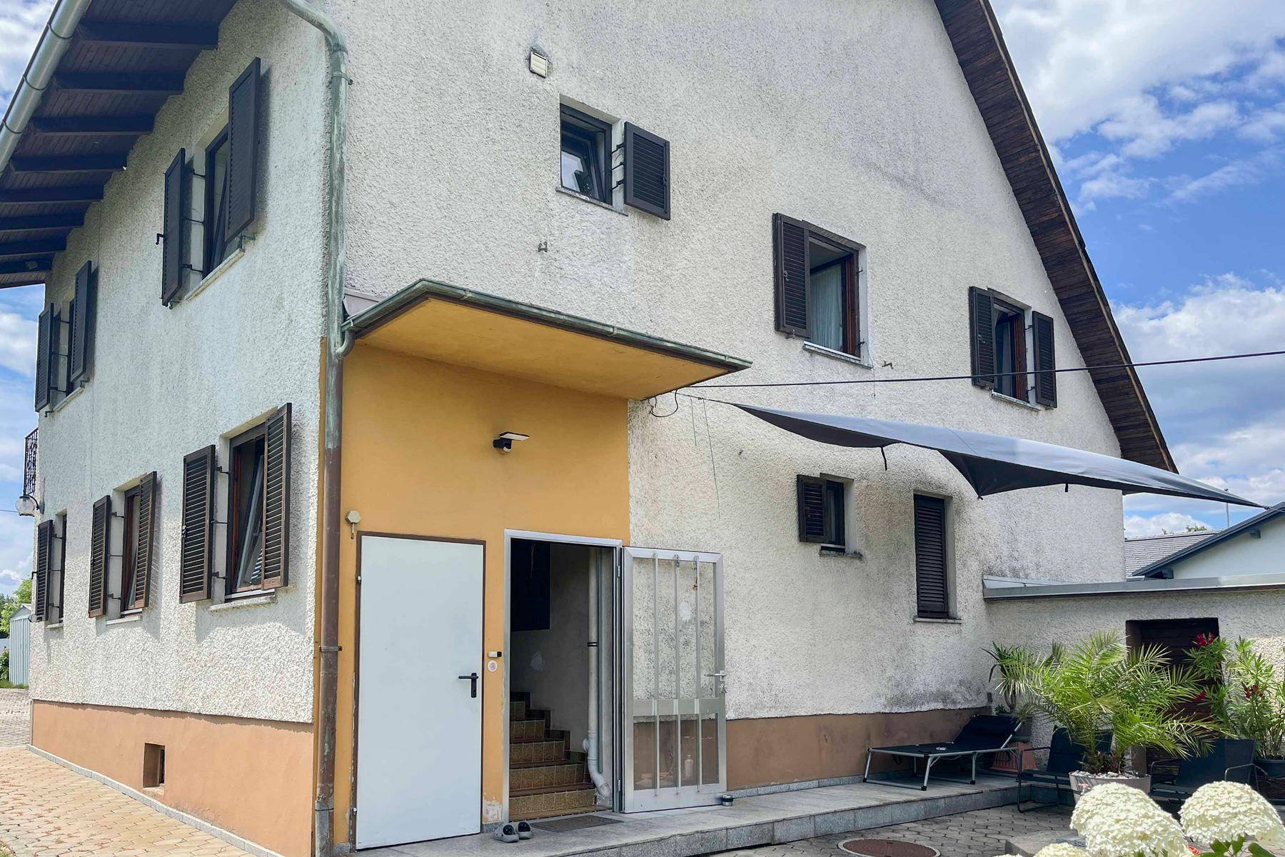 Seitenansicht des Hauses mit Eingangsbereich, Fensterläden und einer kleinen Terrasse.