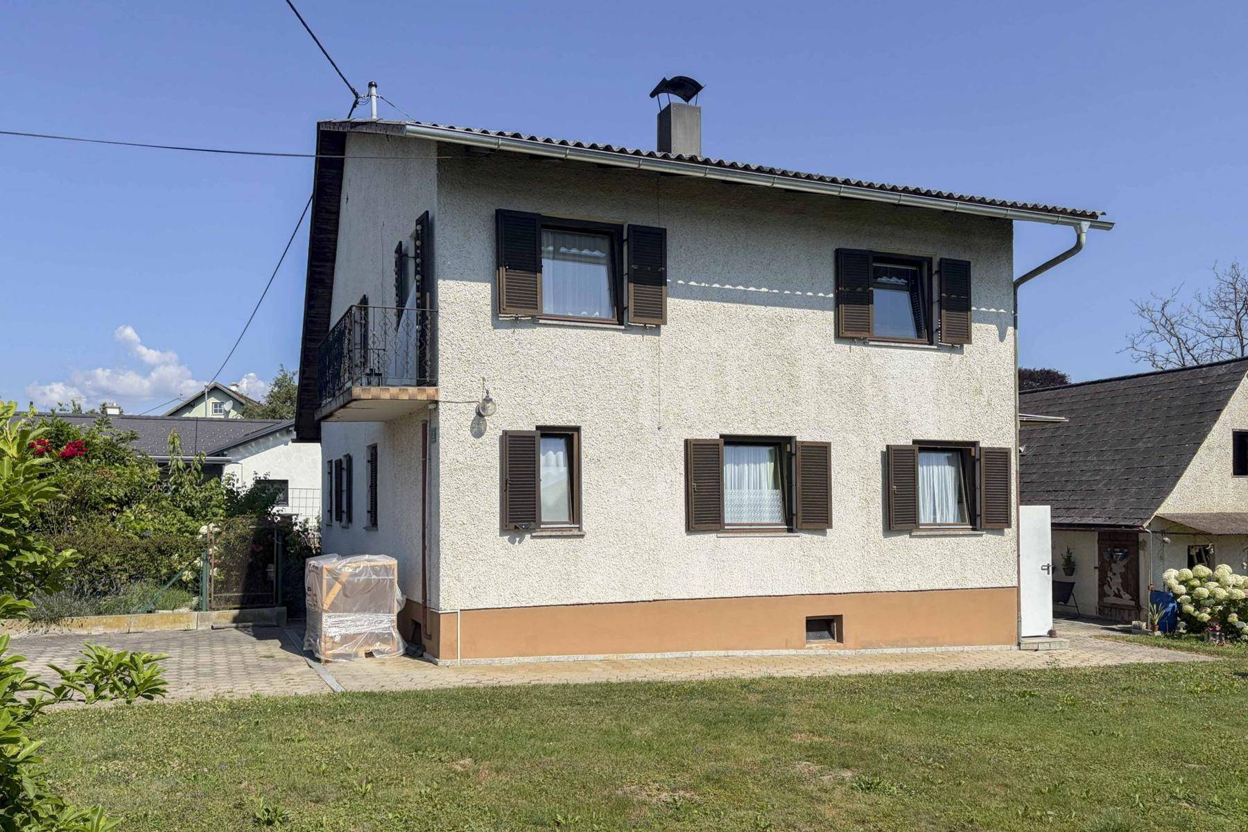 Rückansicht des Hauses mit Rasenfläche, Fensterläden und kleinem Balkon.