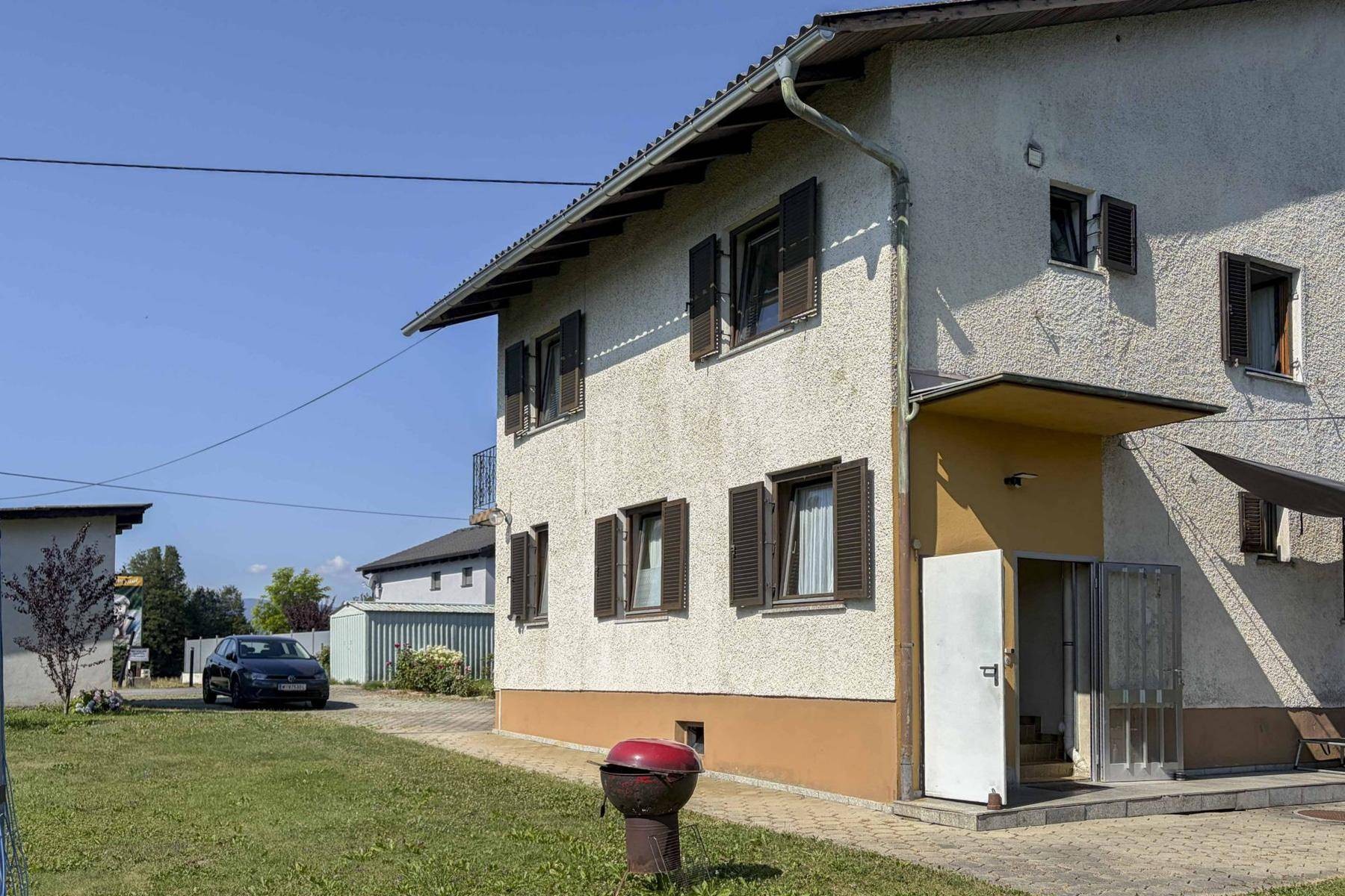 Seitenansicht des Hauses mit Rasenfläche, Grill und gepflasterter Zufahrt.
