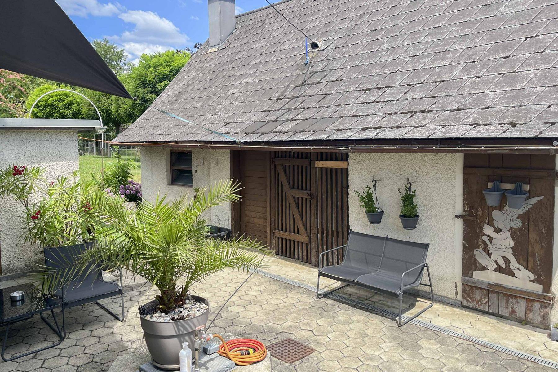 Gepflasterte Terrasse mit Gartenmöbeln und Blick auf ein Nebengebäude.