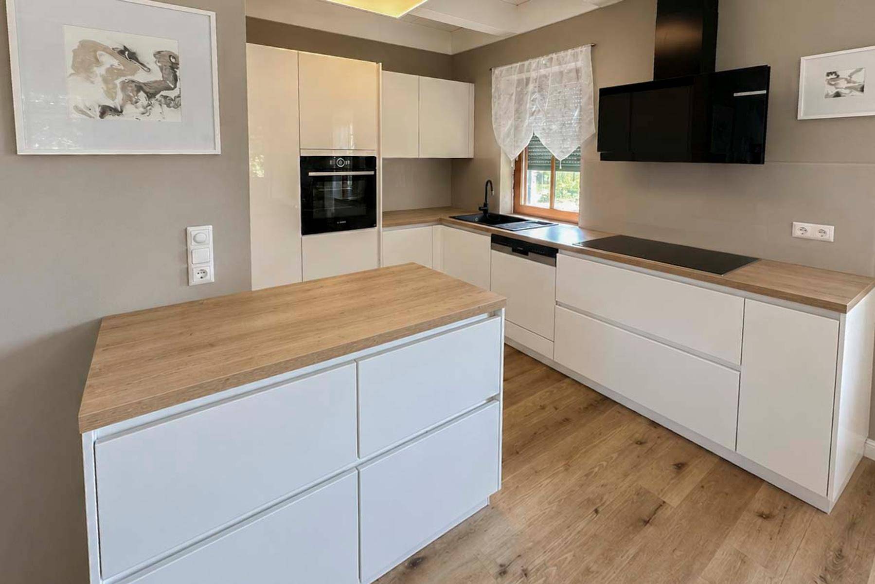 Moderne weiße Küche mit Holz-Arbeitsplatten, Kochinsel und integrierten Geräten.