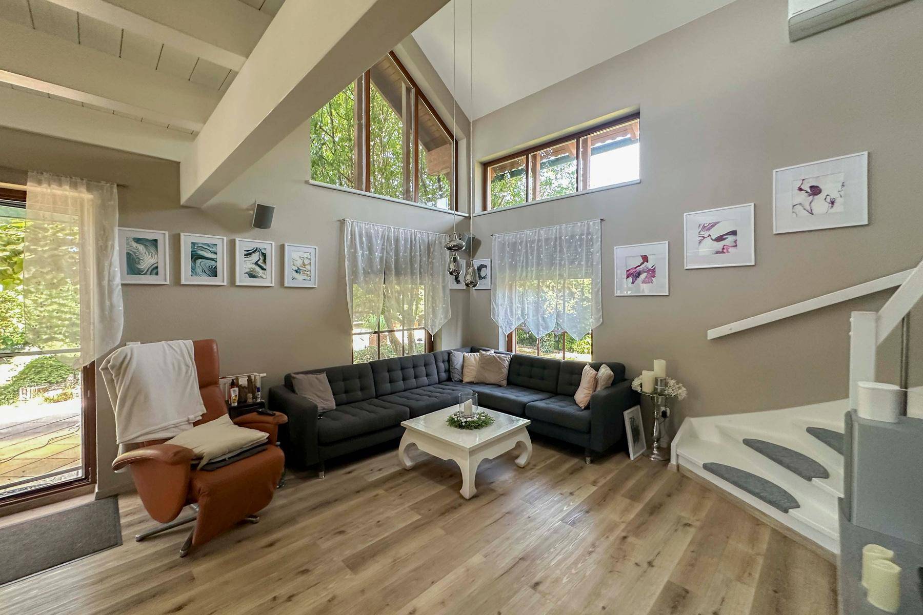 Geräumiges Wohnzimmer mit hoher Decke, großen Fenstern und Zugang zum Außenbereich.