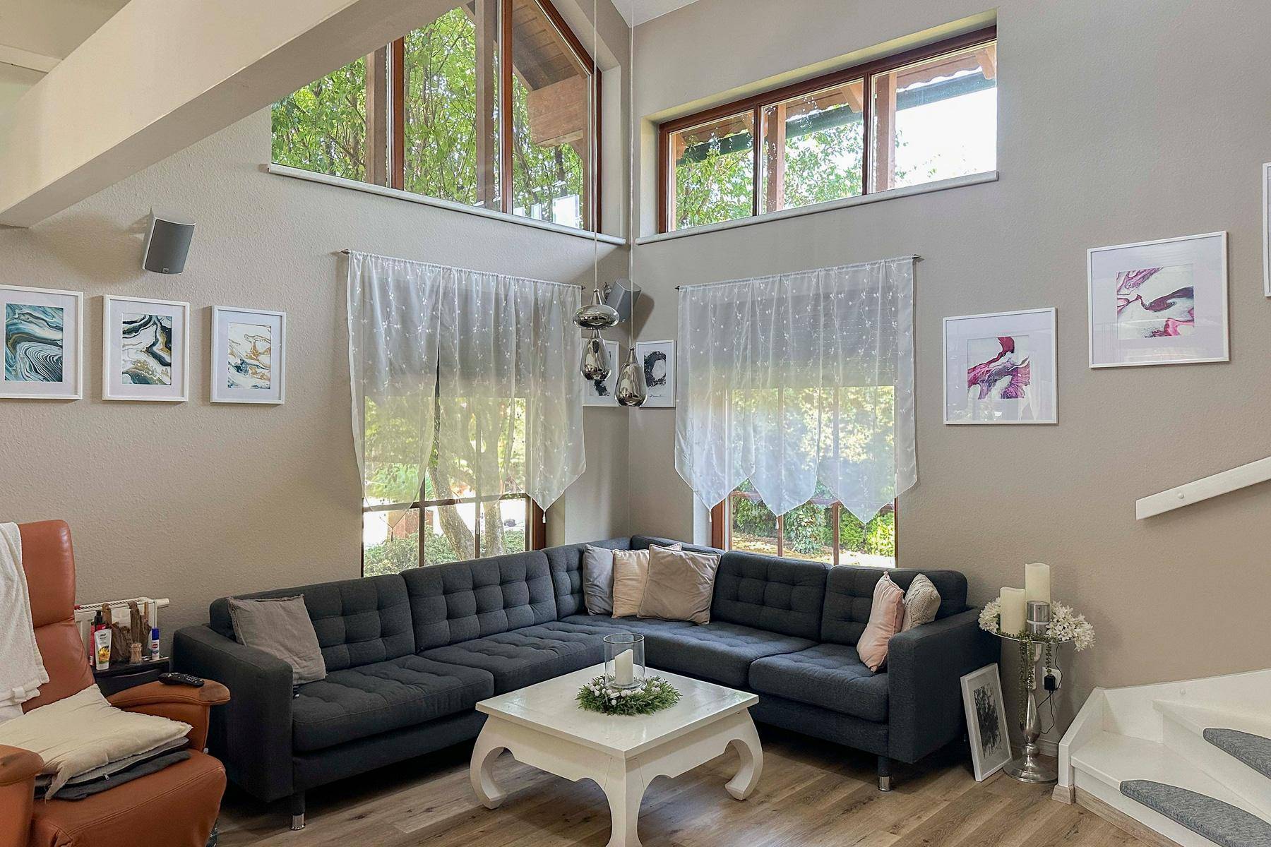 Helles Wohnzimmer mit hoher Decke, großen Fenstern und gemütlicher Eckcouch.