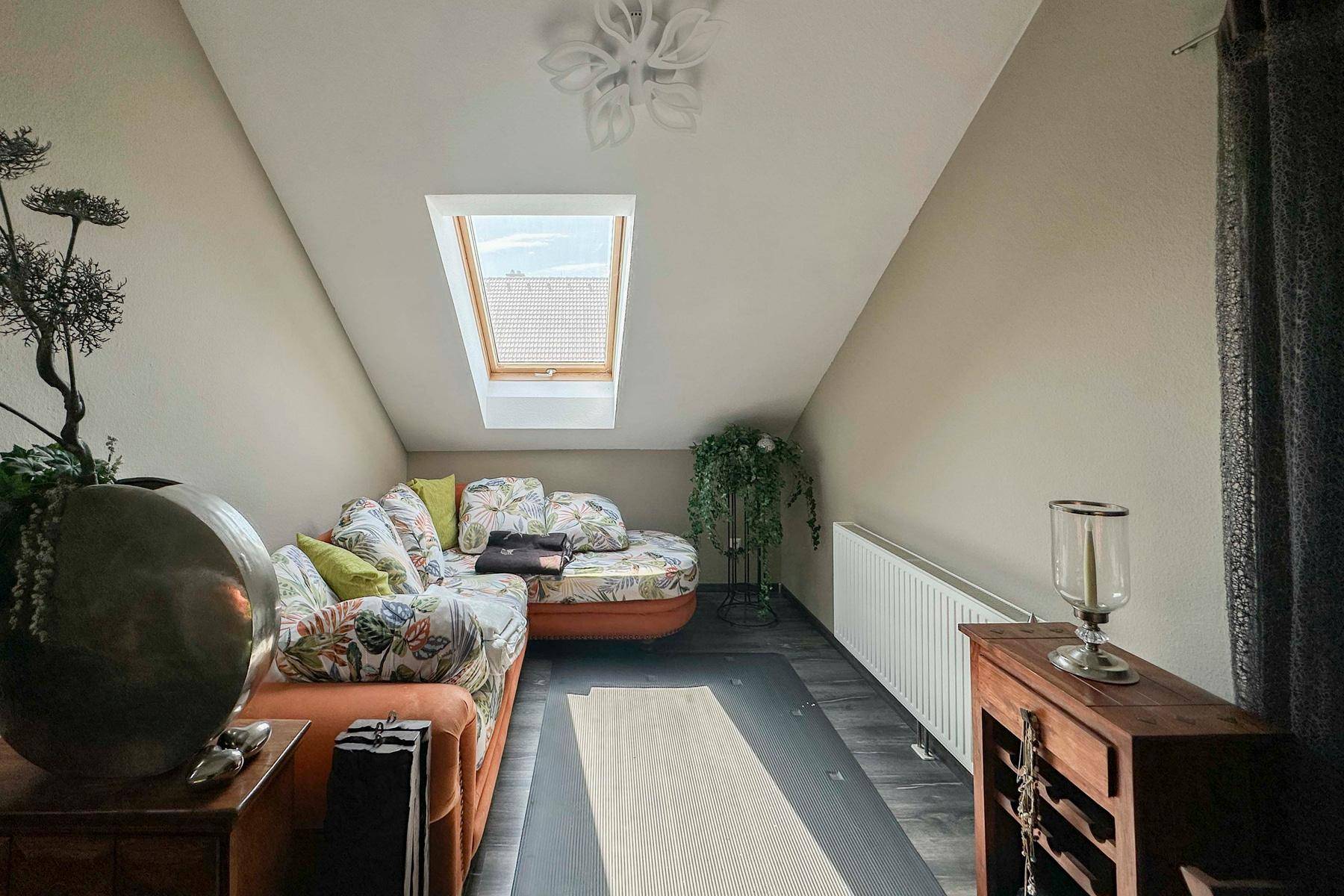 Gemütlicher Dachraum mit Schlafcouch, Dachfenster und Holzboden.