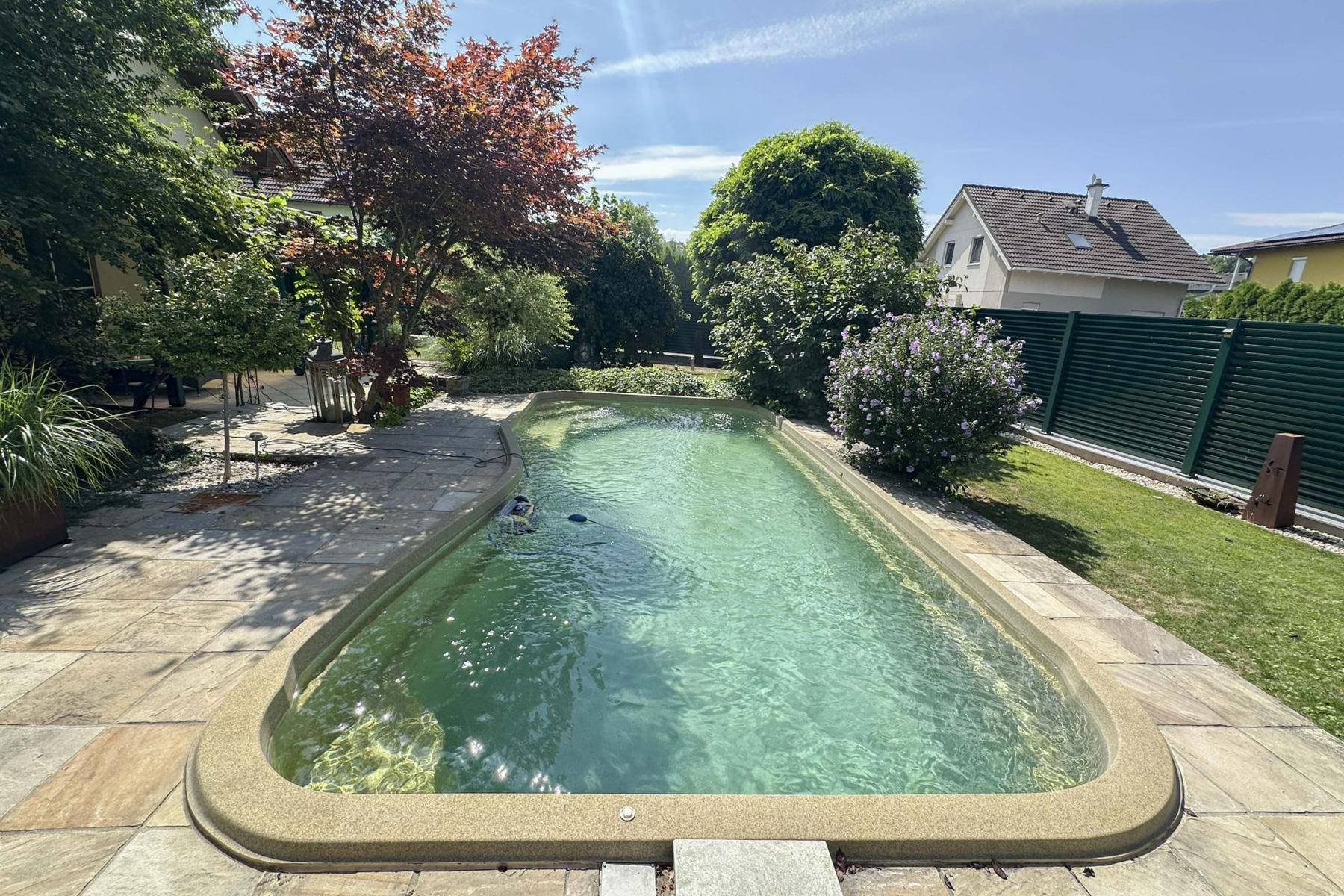 Großer Garten mit Swimmingpool und gepflegter Grünfläche unter blauem Himmel.