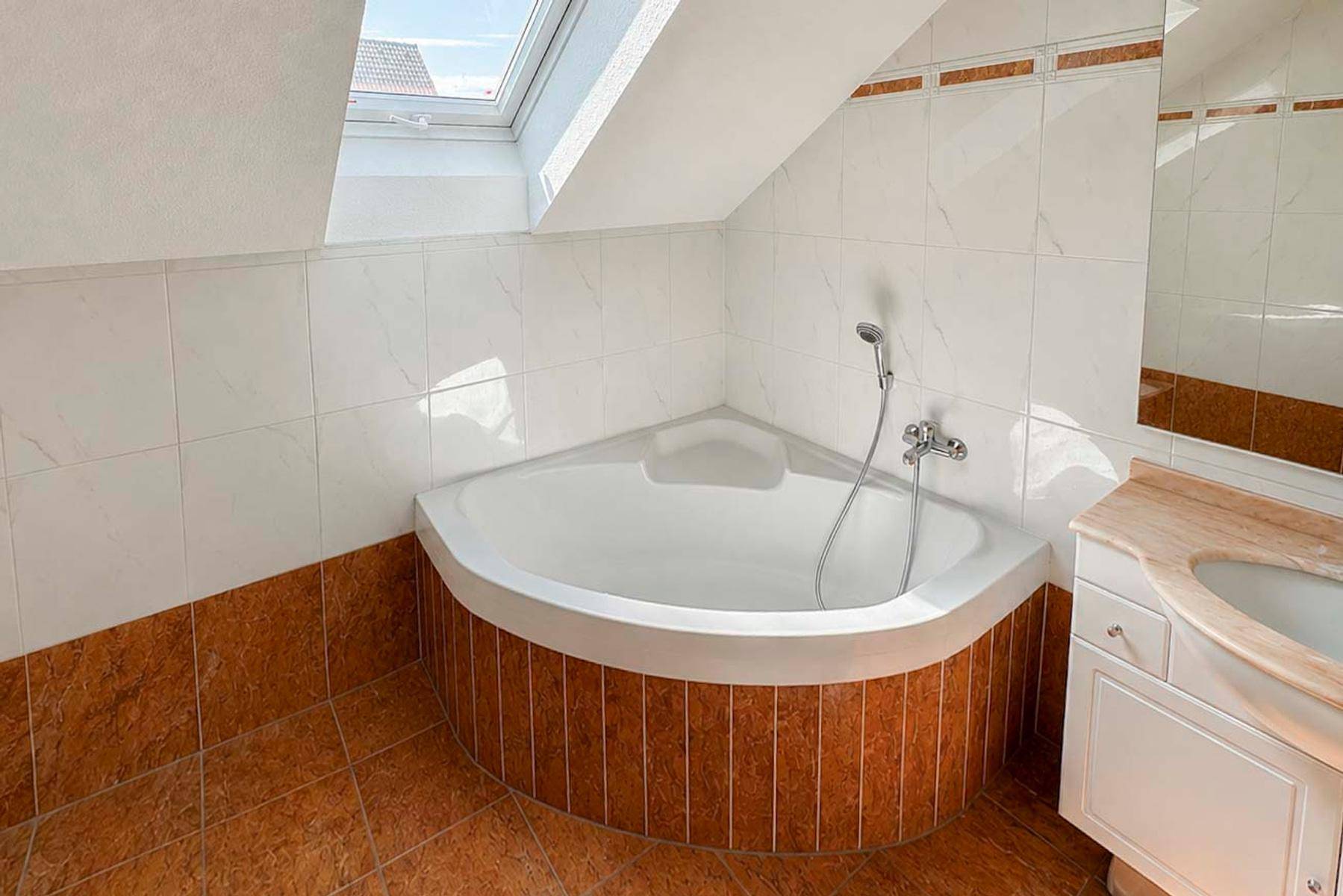 Badezimmer mit Eckbadewanne, Dachfenster und Fliesen in warmen Farbtönen.