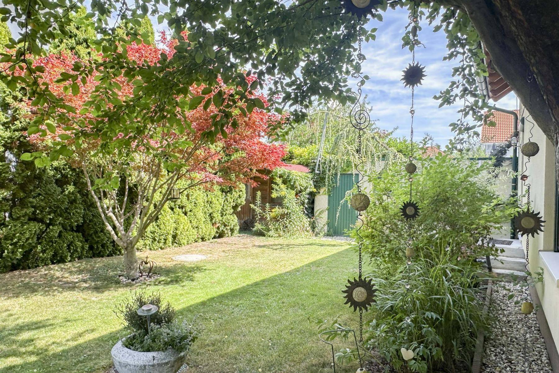 Gepflegter Garten mit Rasenfläche, Bäumen und dekorativen Elementen.