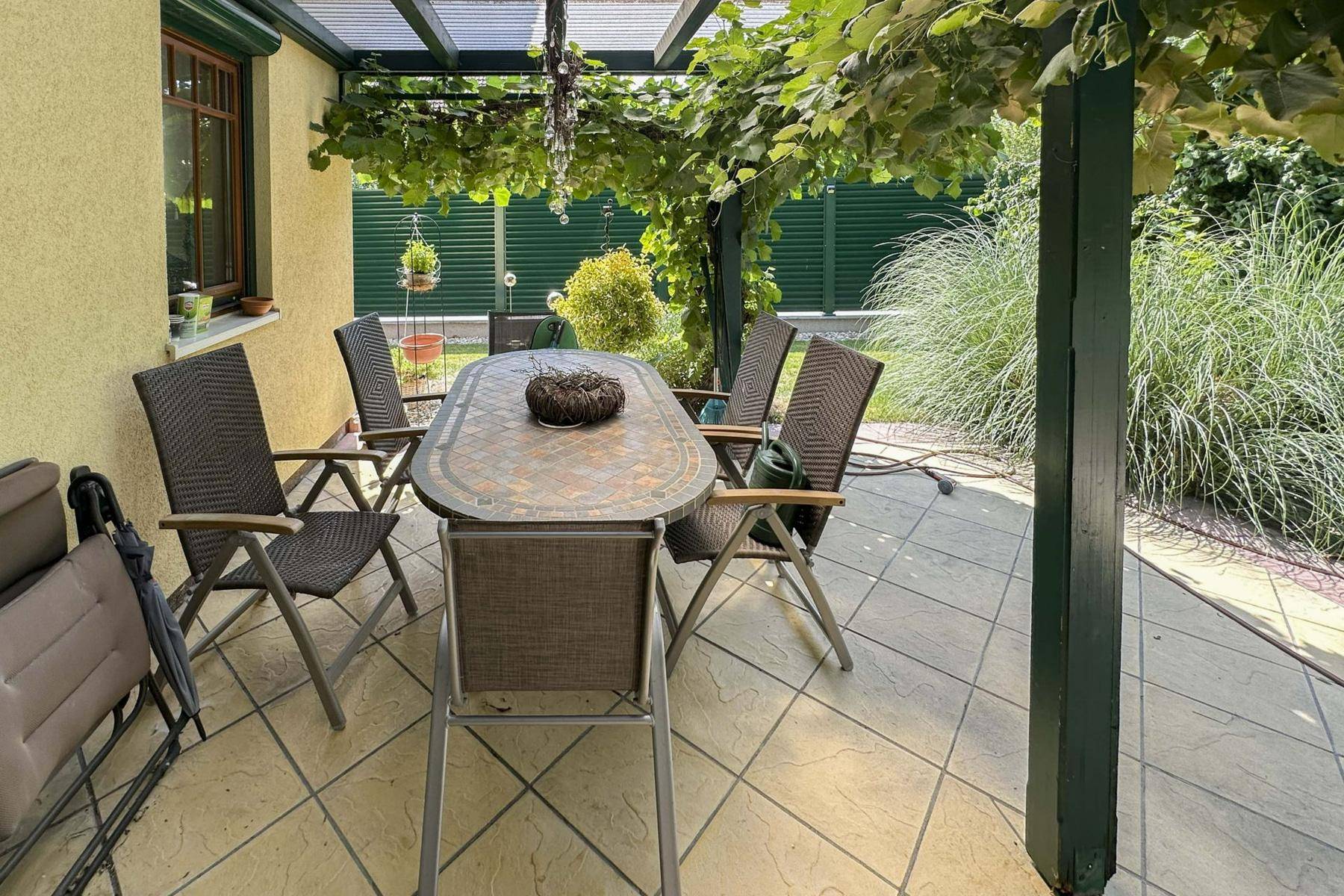 Überdachte Terrasse mit Gartenmöbeln und Weinreben, ideal für Mahlzeiten im Freien.