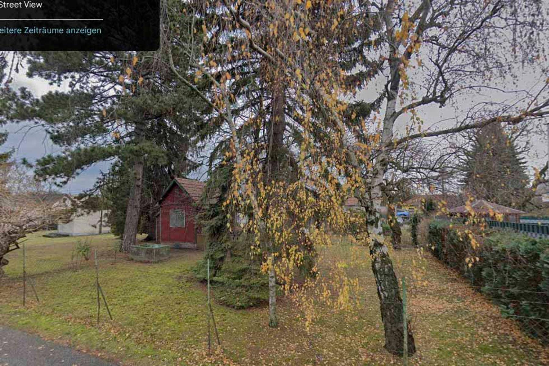 Blick von der Straße auf ein kleines rotes Gebäude umgeben von Bäumen und Herbstlaub.