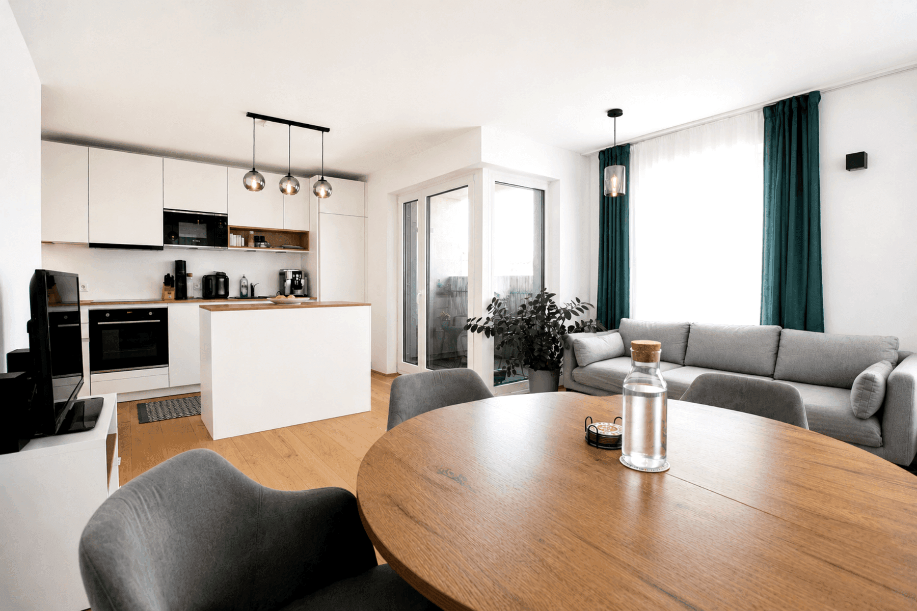 Heller offener Wohn-Essbereich mit moderner Küche, Holzboden und Zugang zum Balkon.