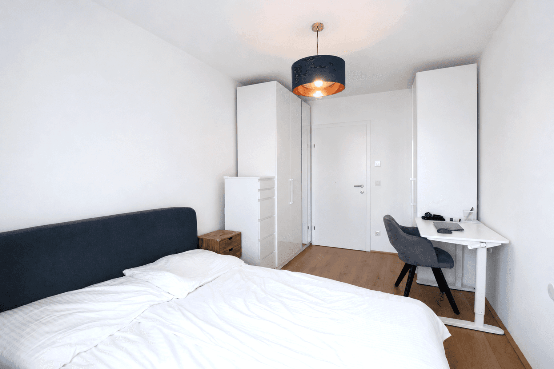 Modernes Schlafzimmer mit Holzboden, weißem Kleiderschrank und Schreibtisch.