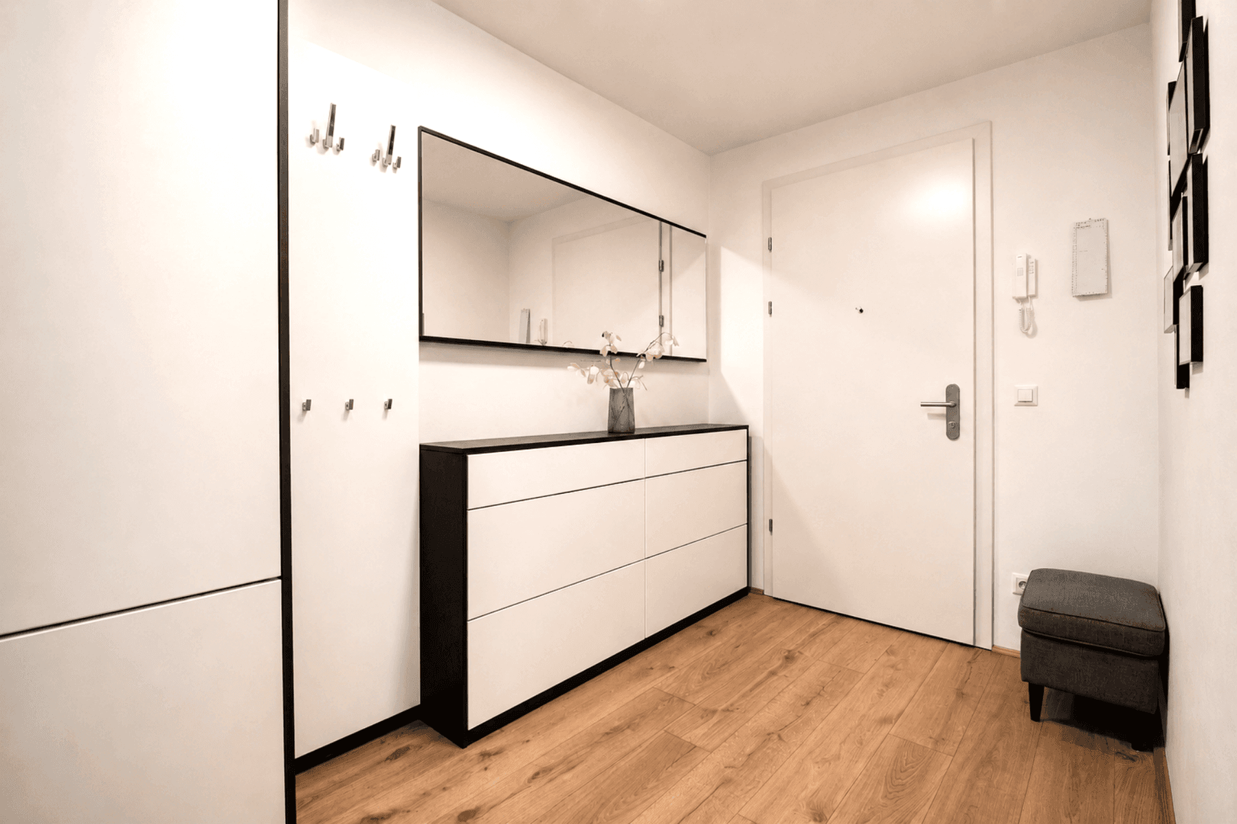 Heller Eingangsbereich mit Holzboden, Garderobe und großem Spiegel.