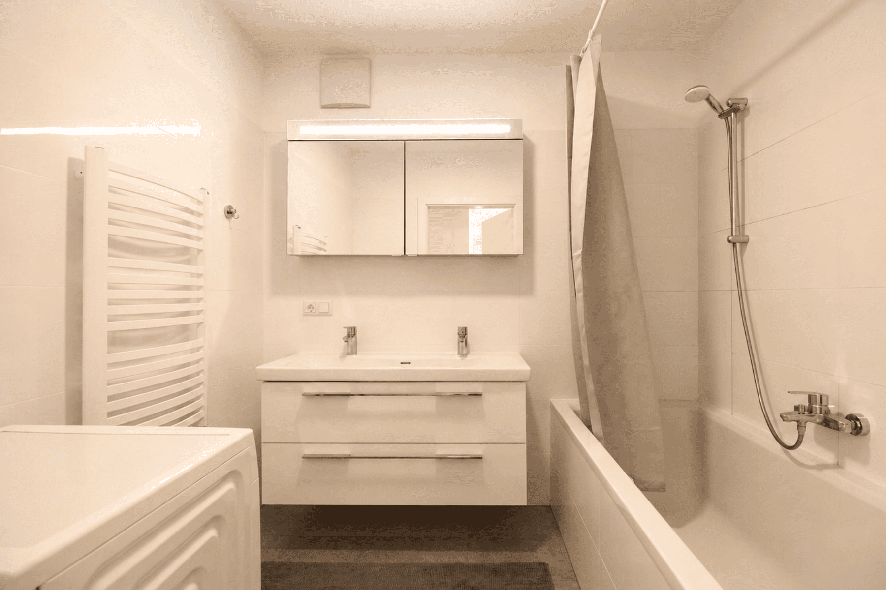 Helles Badezimmer mit Doppelwaschbecken, Badewanne und beheiztem Handtuchhalter.