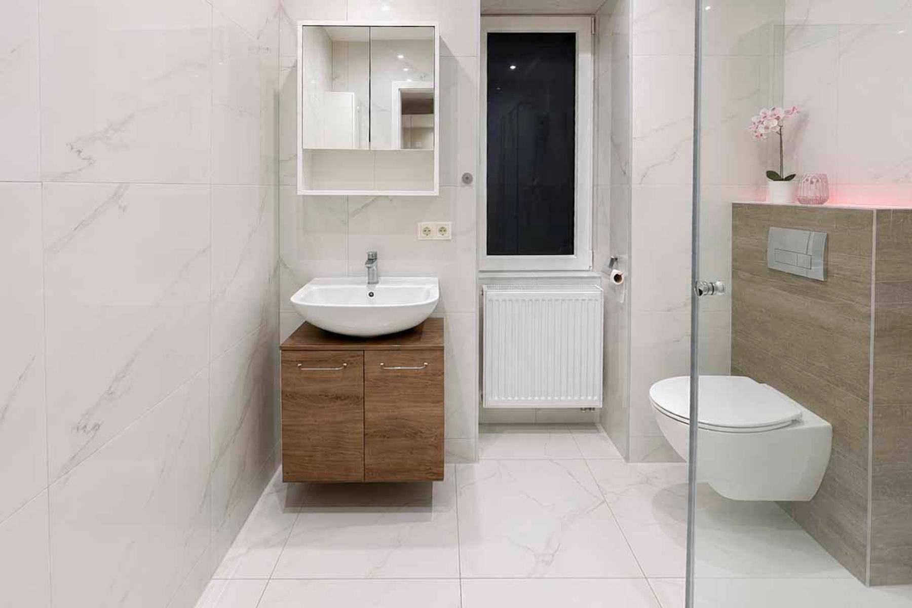 Modernes Badezimmer mit weißen Marmorfliesen, Waschtisch und wandhängendem WC.