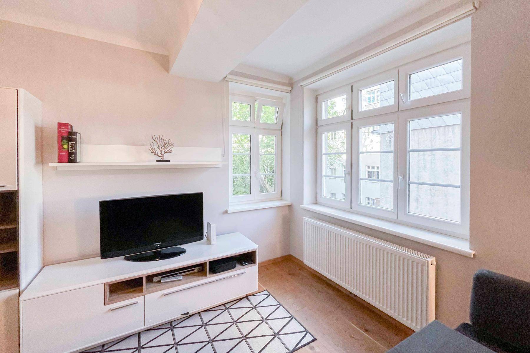 Gemütliches Wohnzimmer mit Holzboden und Heizkörper unter den großen Fenstern.