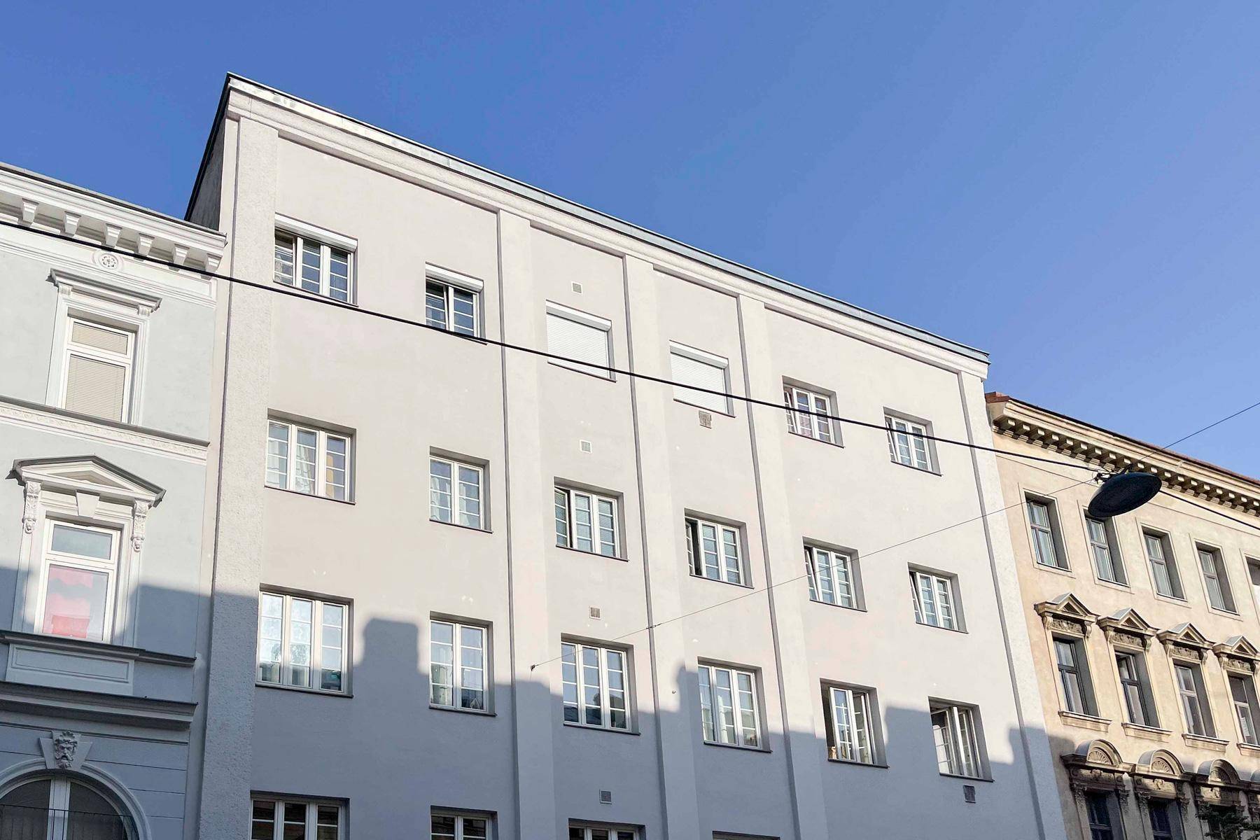 Fassade eines Mehrfamilienhauses mit vielen Fenstern unter blauem Himmel.