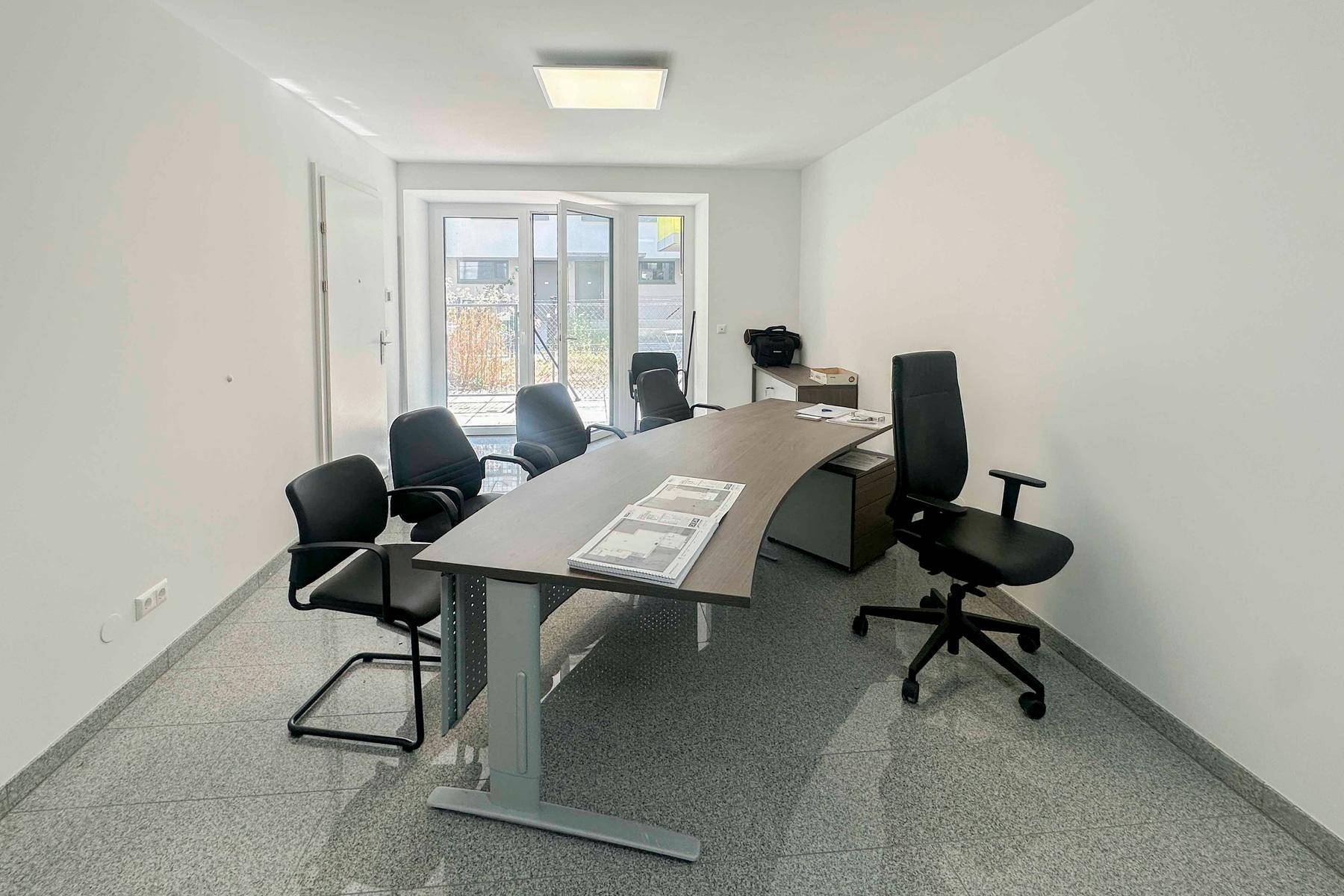 Moderner Büroraum mit großem Schreibtisch und mehreren Stühlen, ideal für Besprechungen.