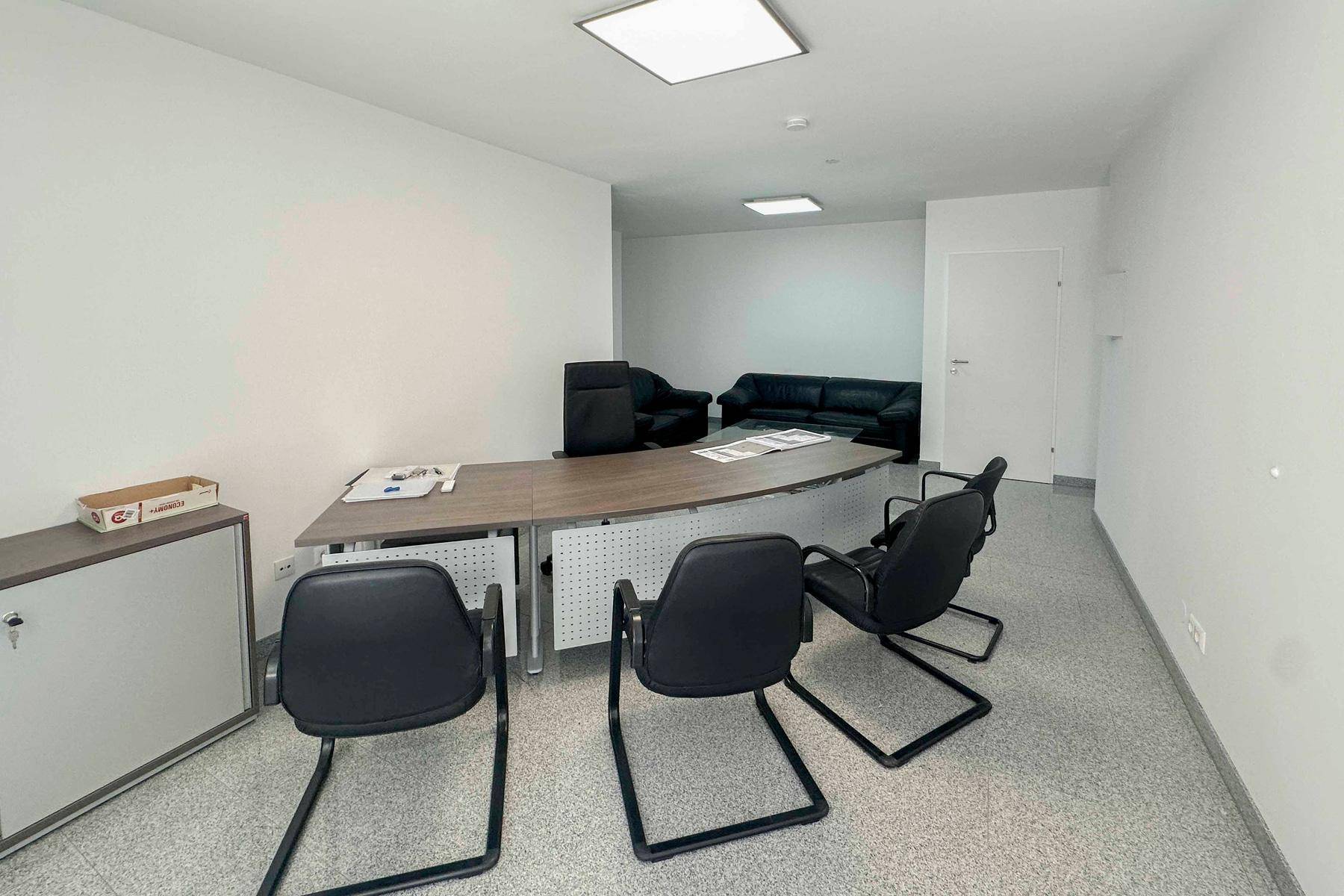 Geräumiger Büroraum mit Schreibtisch, Stühlen und einer Sitzecke im Hintergrund.