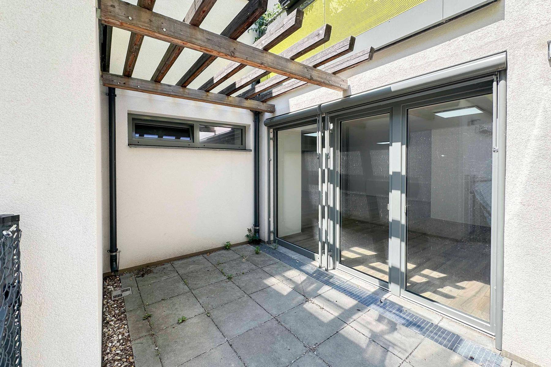 Kleine gepflasterte Terrasse mit Holzpergola und Zugang zum Innenbereich.