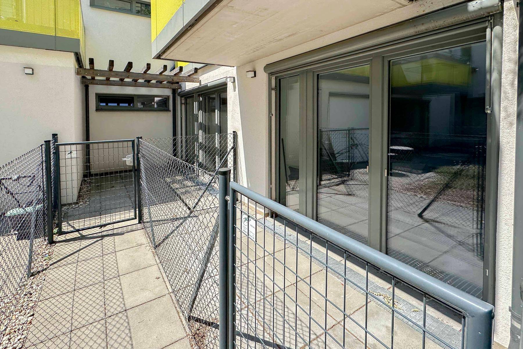 Außenbereich mit gepflasterter Terrasse, Zaun und Blick auf die umliegenden Gebäude.
