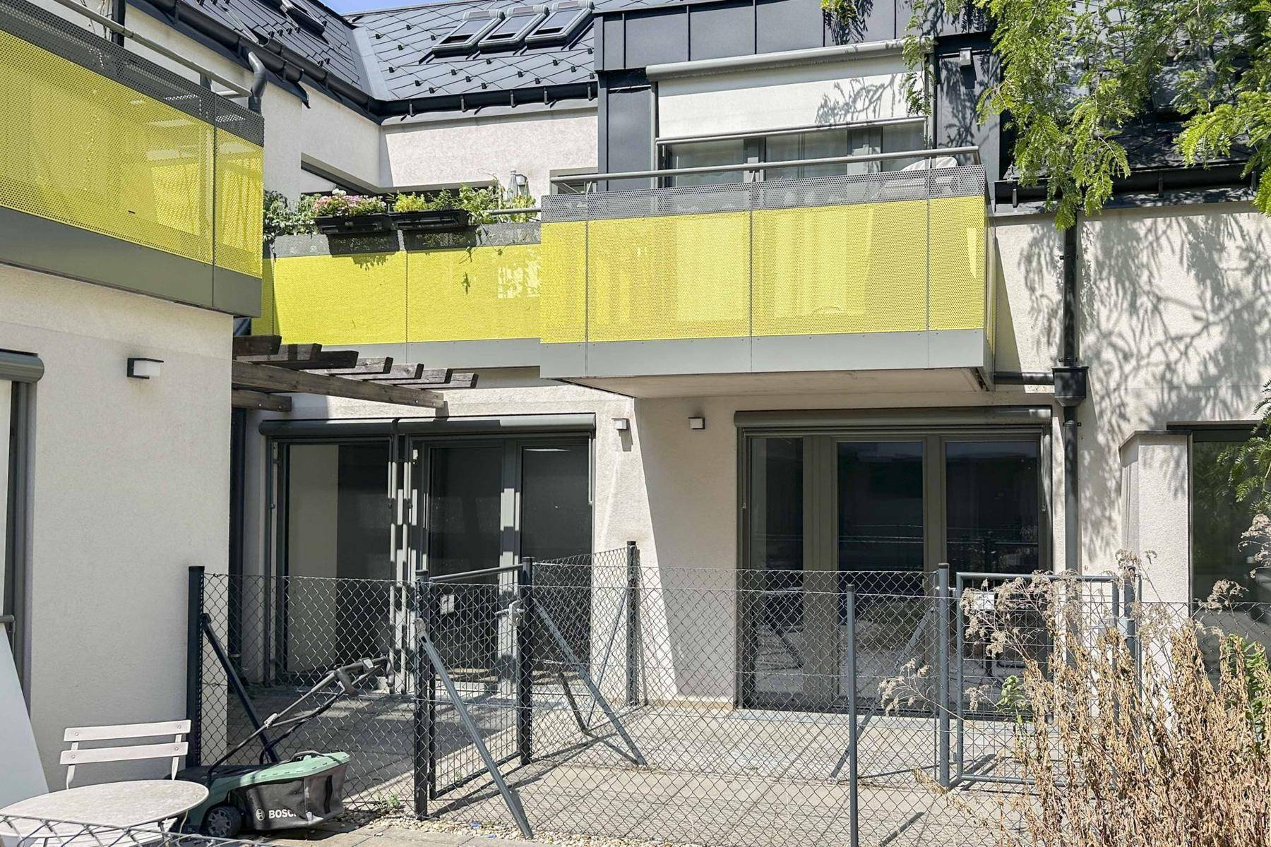Mehrere Terrassen und Balkone mit gelben Glasbrüstungen an der Gebäuderückseite.
