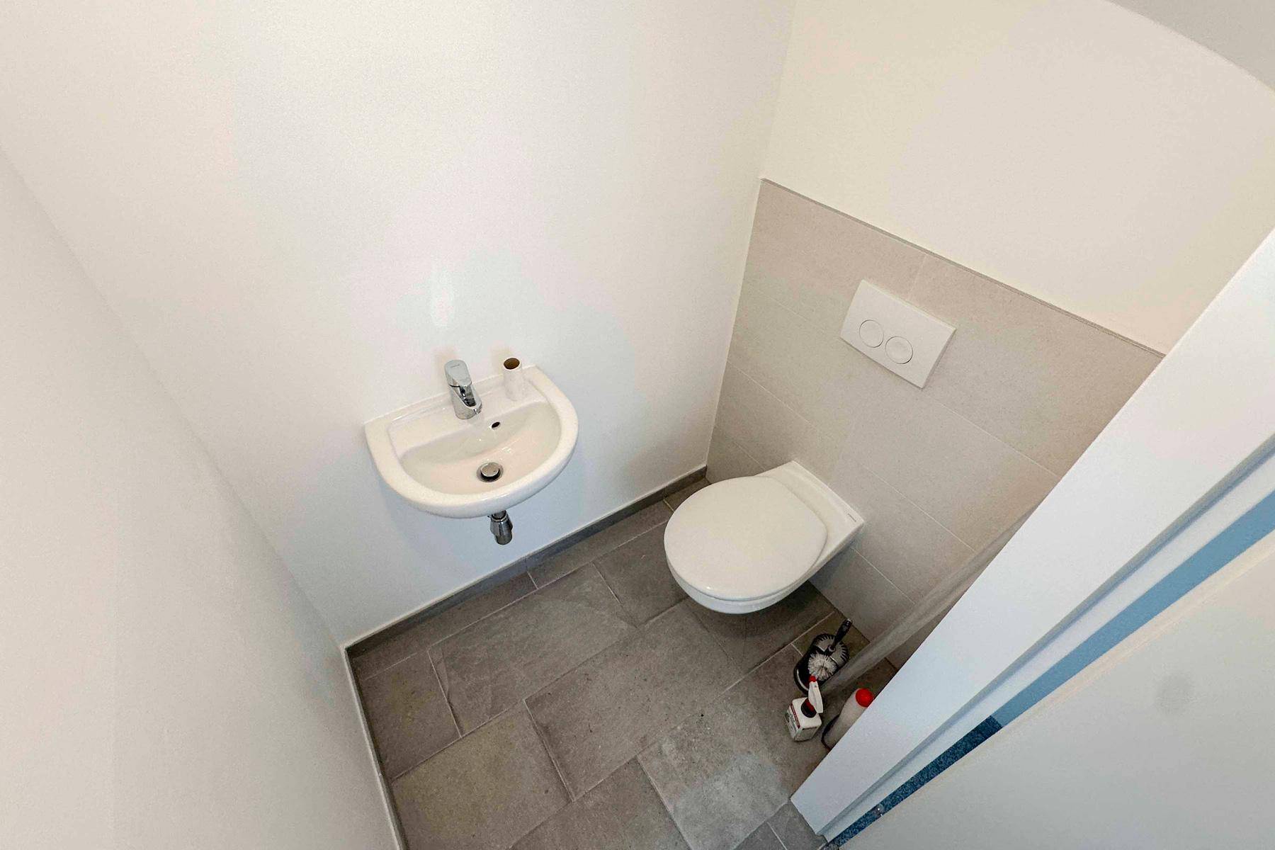 Modernes Gäste-WC mit Wand-WC und kleinem Waschbecken, hell gefliest.
