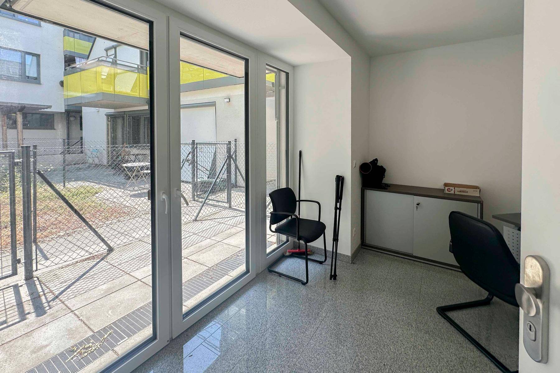 Kleiner Büroraum mit großen Fenstern und Blick auf den Außenbereich.