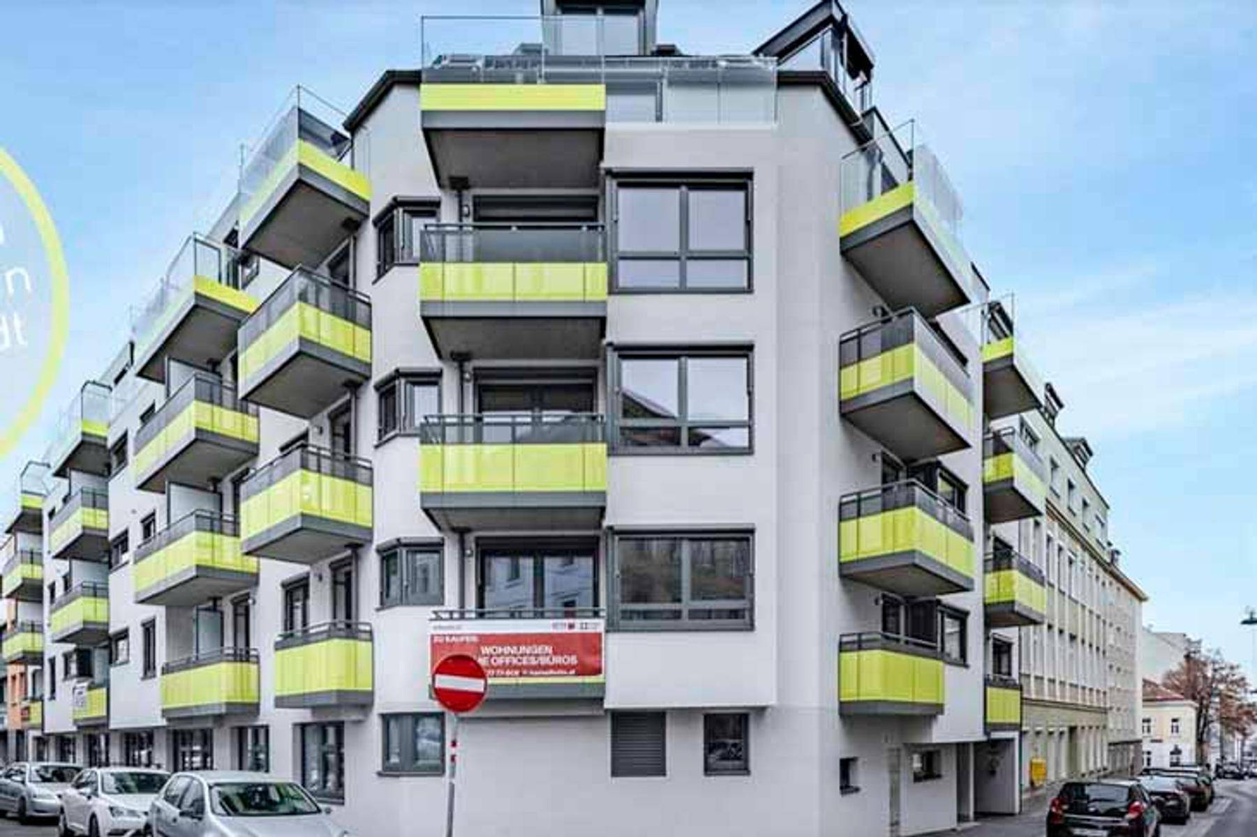Modernes Mehrfamilienhaus mit vielen Balkonen und gelben Akzenten an der Fassade.