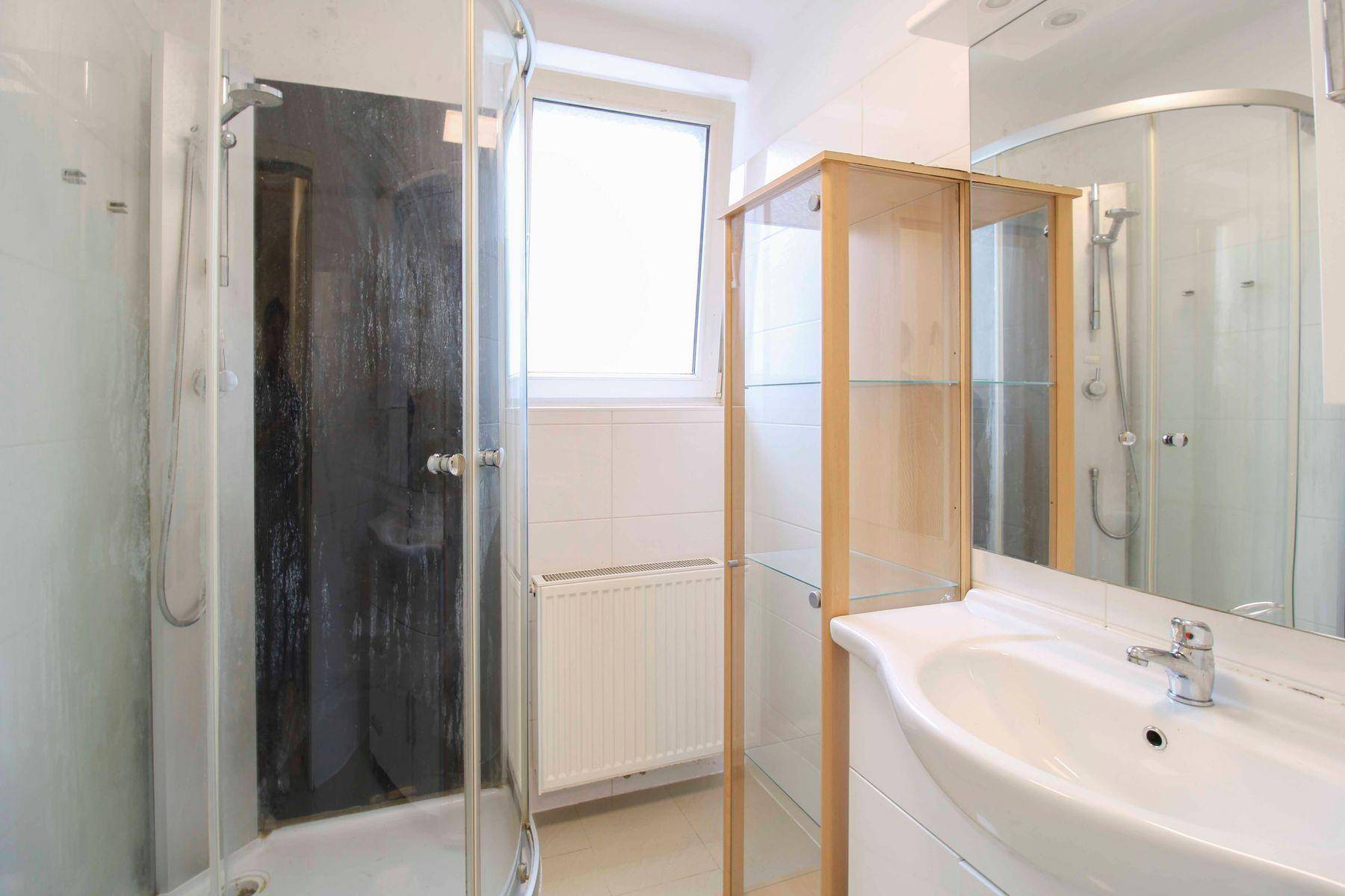 Helles Badezimmer mit Duschkabine, Waschbecken, Spiegel und Fenster für natürliche Belüftung.