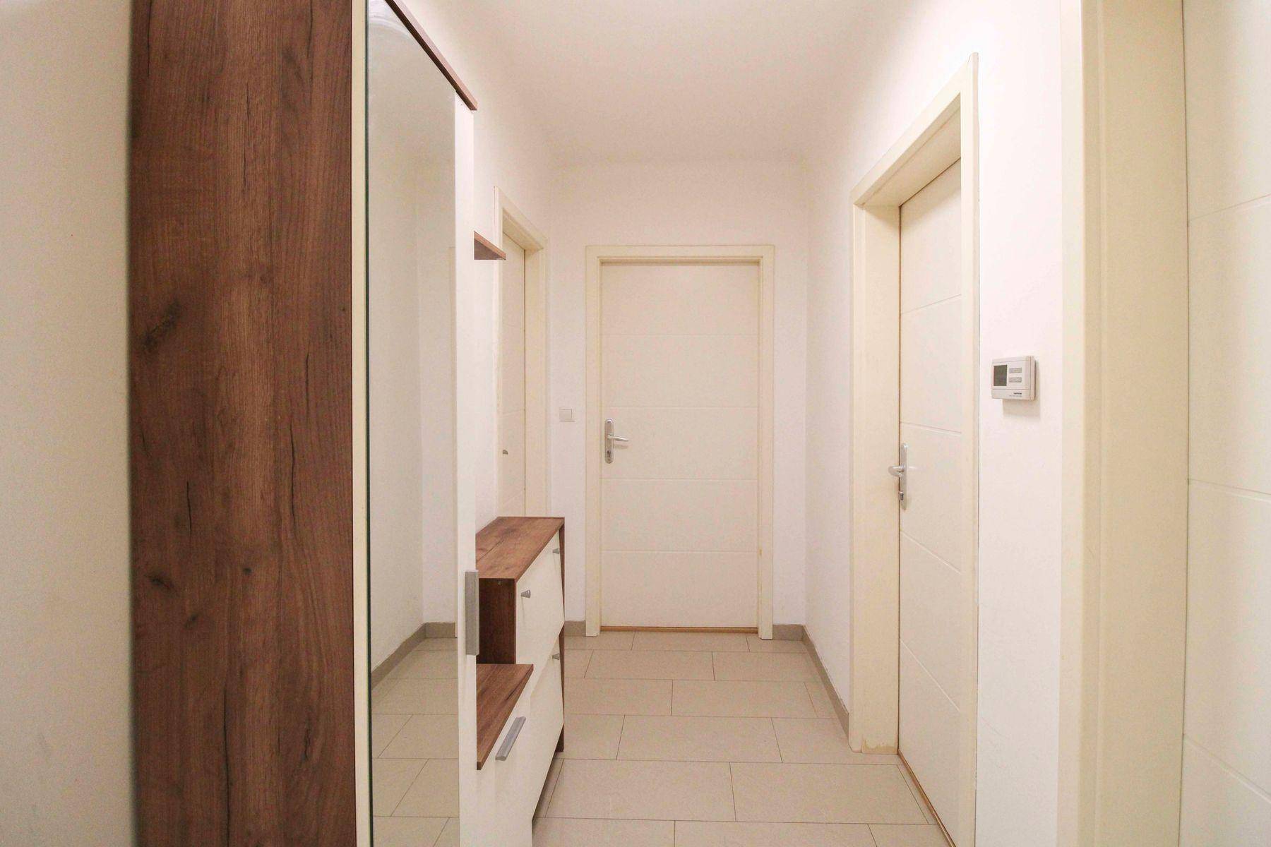 Heller Flur mit Fliesenboden, Holzschrank mit Spiegel und Zugang zu mehreren Zimmern.