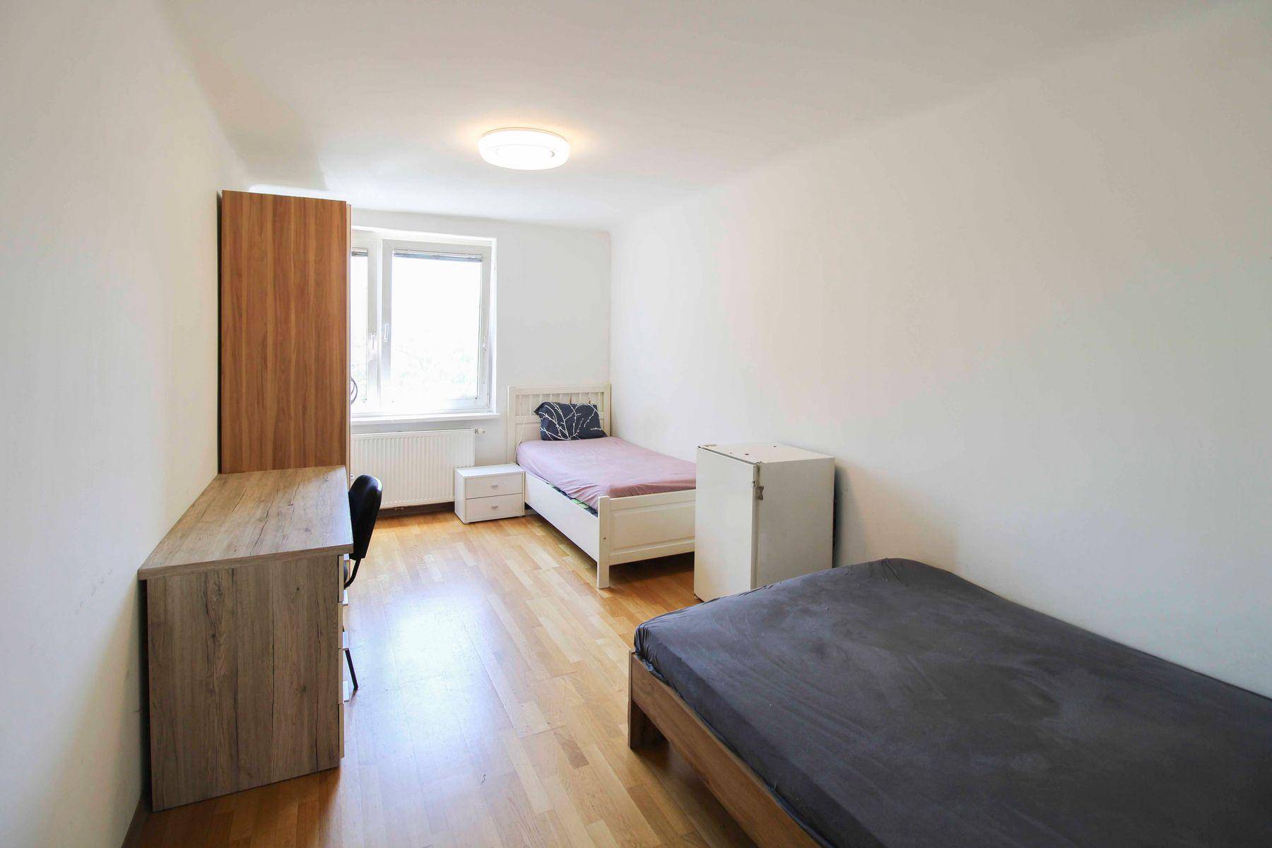 Gemütliches Schlafzimmer mit zwei Einzelbetten, Schreibtisch und Kleiderschrank, gut beleuchtet durch ein Fenster.