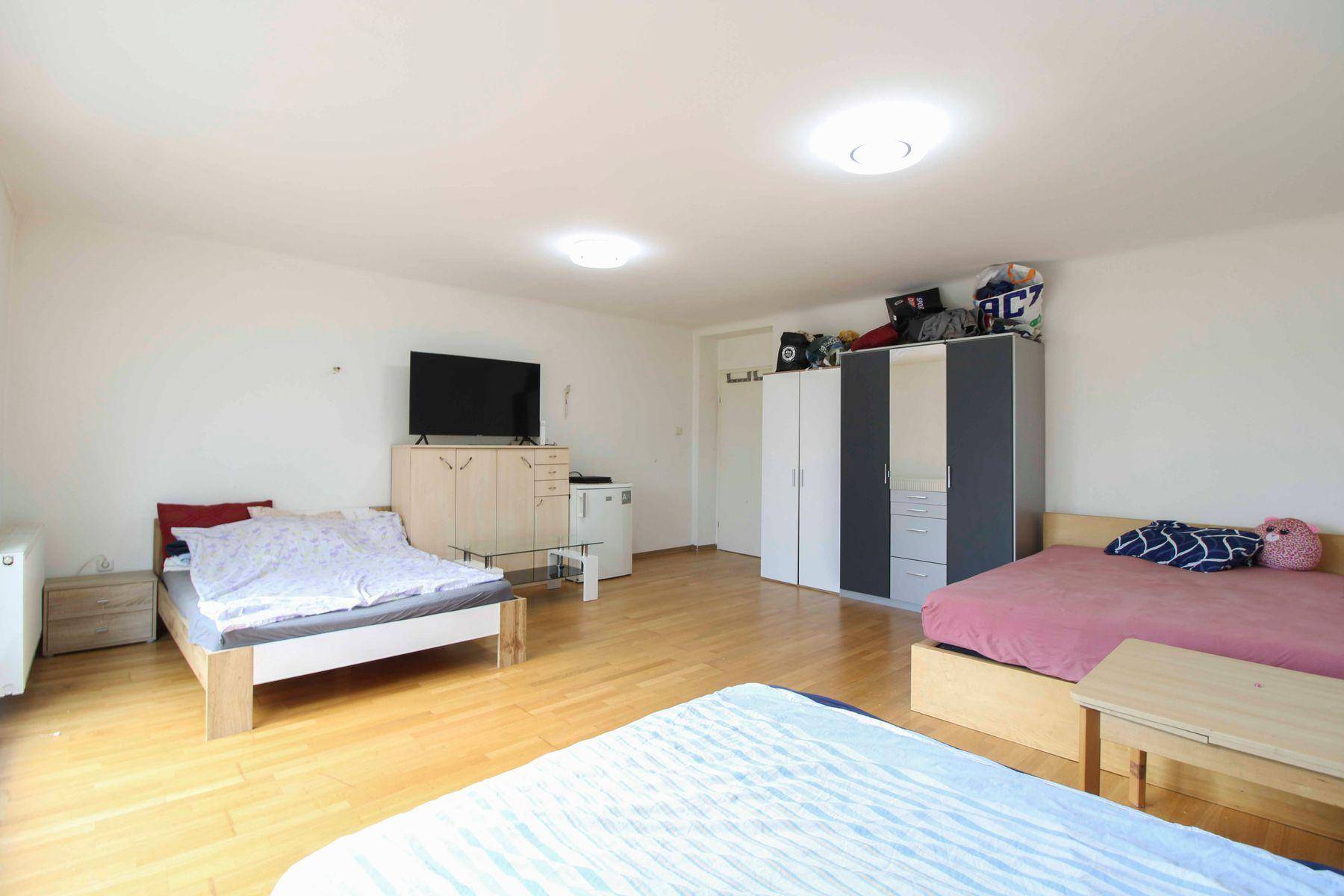Helles Schlafzimmer mit mehreren Betten, Fernseher und Kleiderschränken, ideal für Wohngemeinschaften.